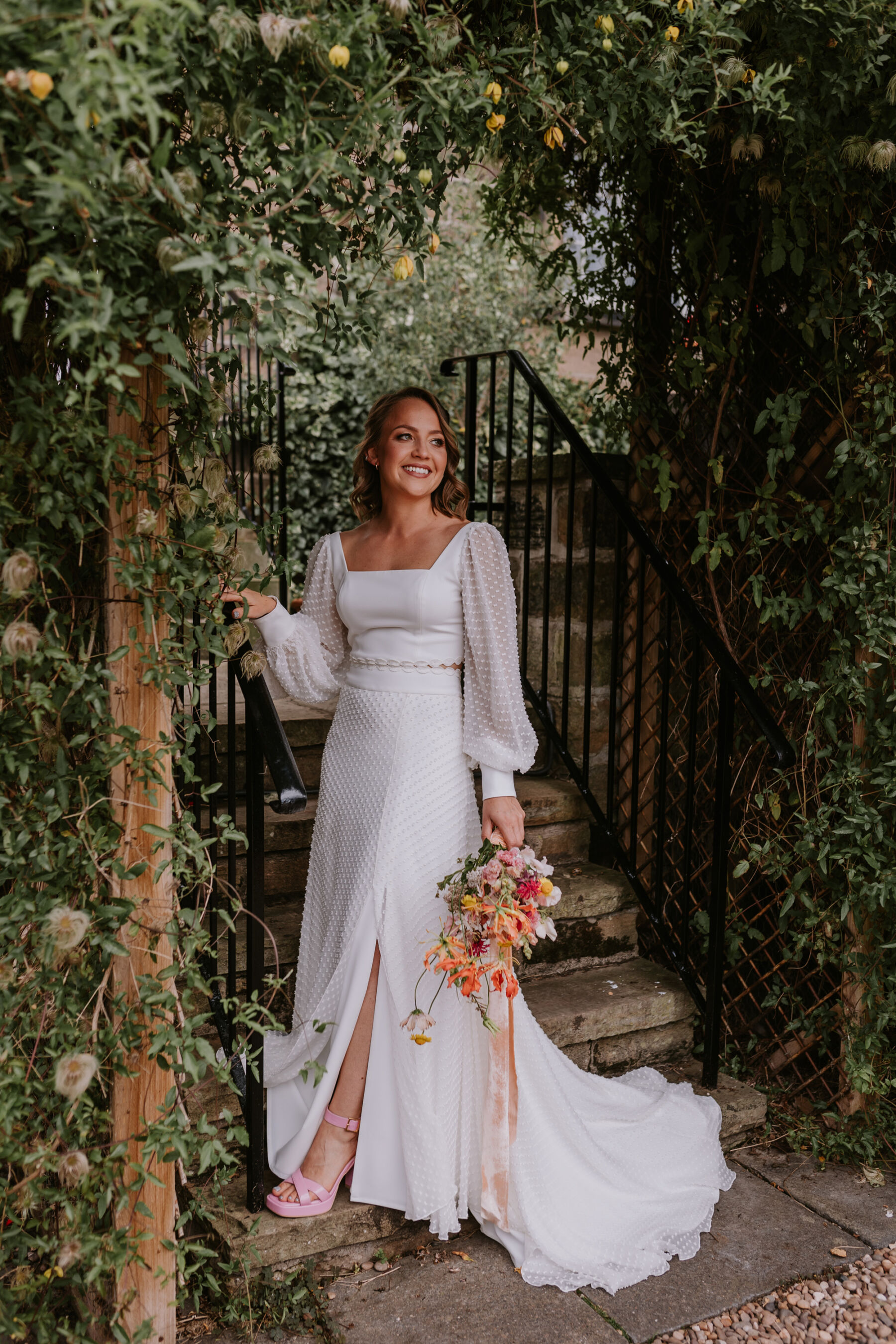 Bride wearing a separate wedding top and skirt. Wedding top has billowed, polka dot sleeves. She carries a colourful wedding bouquet.