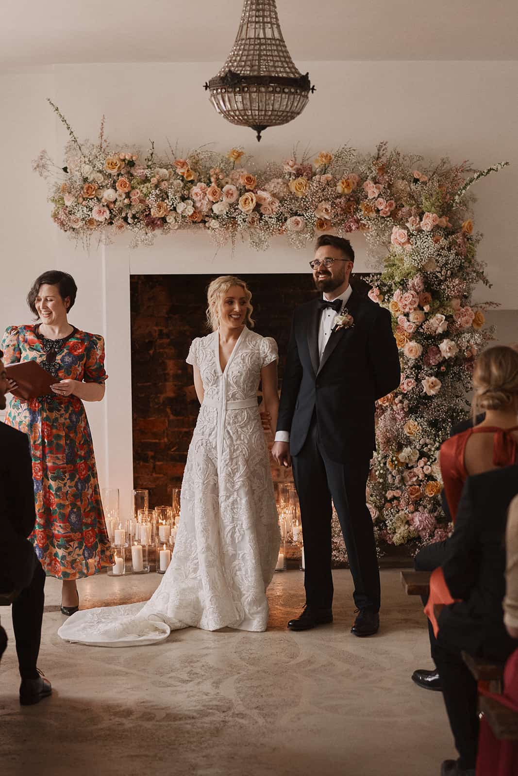 Nat Raybould - Humanist Wedding Celebrant, leading a wedding ceremony by a fireplace surrounded by candles. Benjamin Wheeler Photography.