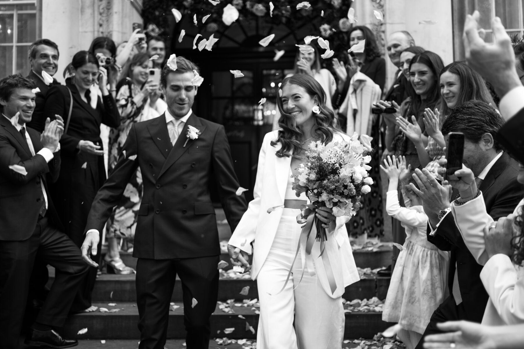 A bride and groom on the famous Chelsea Town Hall steps exiting their wedding ceremony through a confetti tunnel