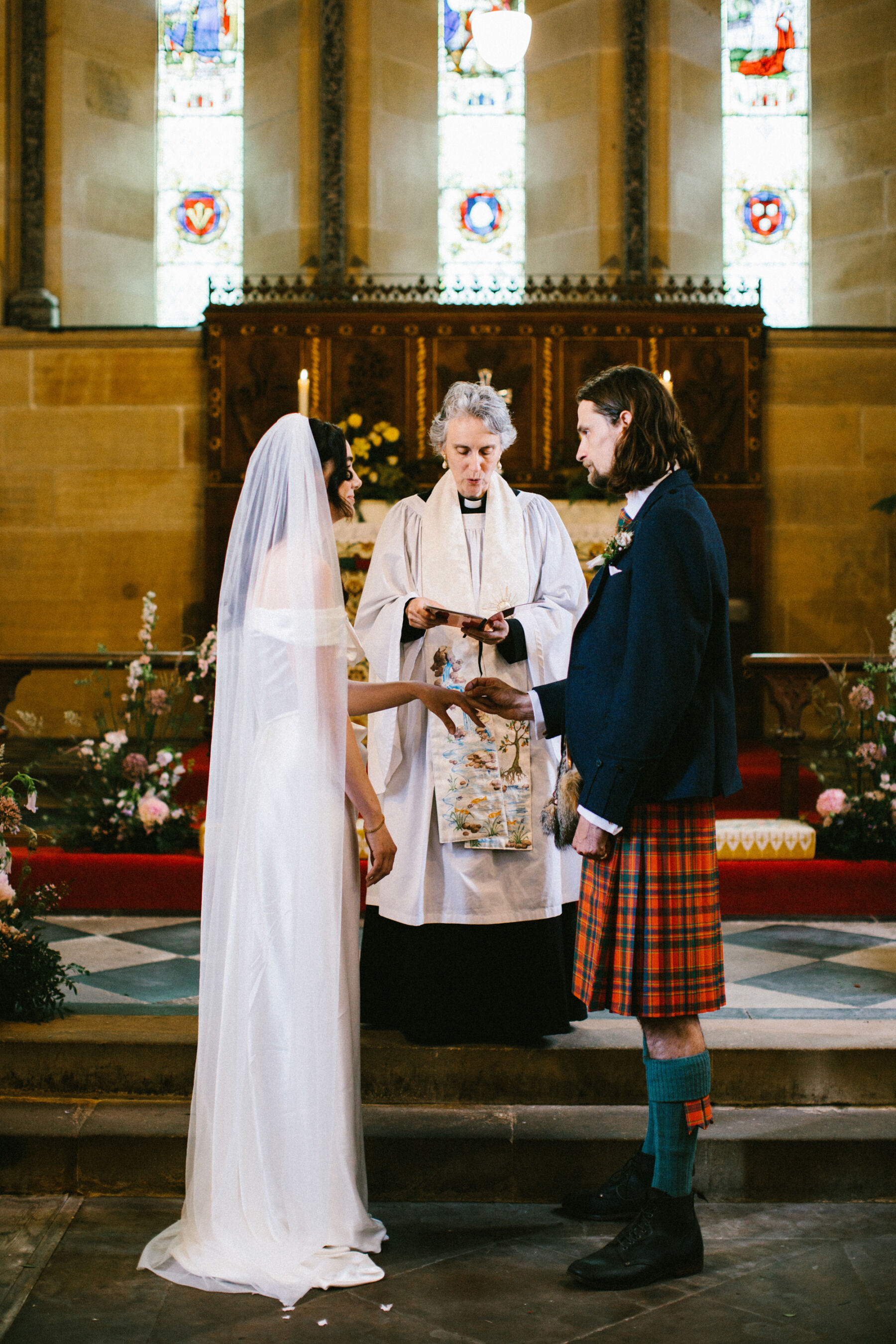 Bride and groom in church. Groom in red tartan kilt, bride in long veil & Vivienne Westwood dress.