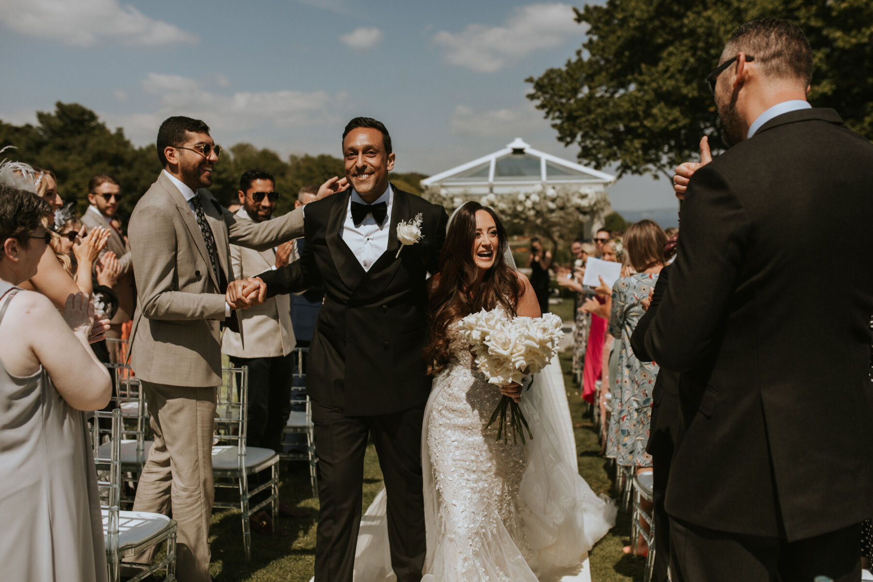 Black tie groom and bride carrying a modern all white wedding bouquet - just married at an outdoor ceremony at The Pennsylvania Castle Estate - a Dorset wedding venue on a clifftop with incredible sea views.