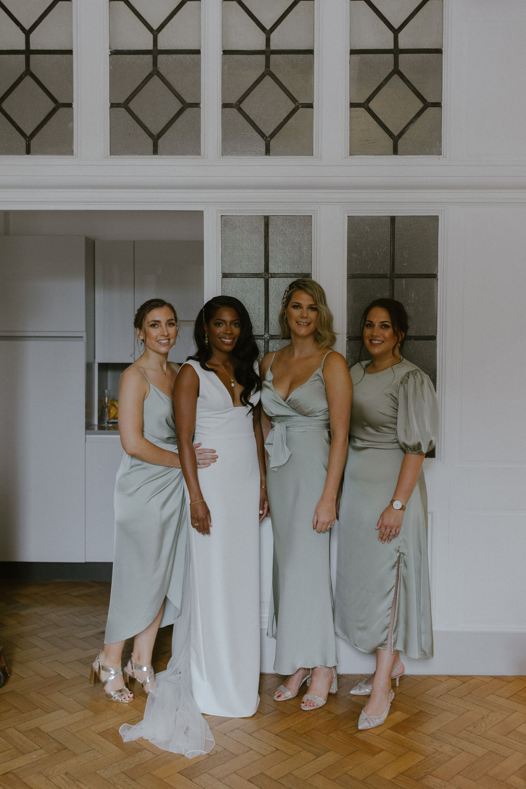 Black bride in a chic, minimalist wedding dress by Sarah Seven, sanding with 3 bridesmaids in sage green dresses. Ruth Atkinson Photography.