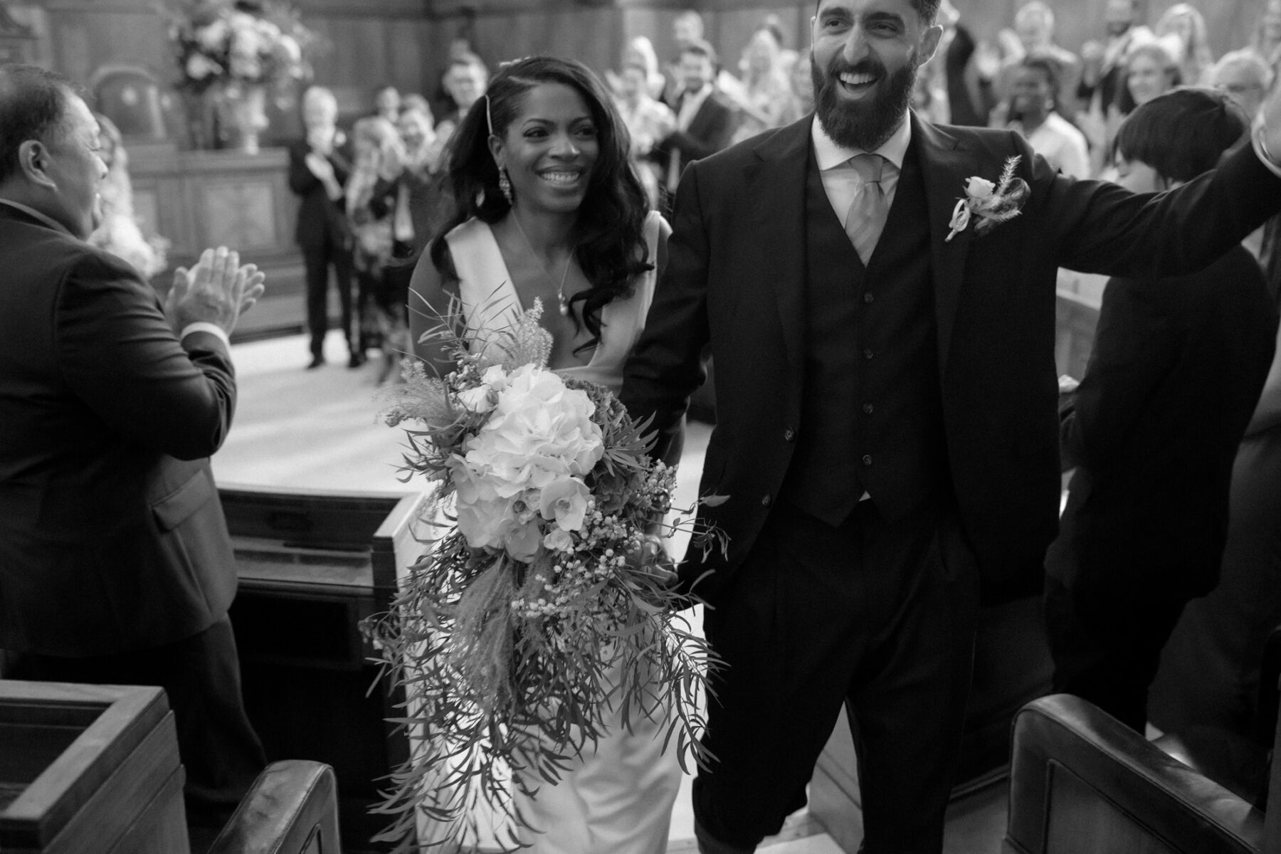 Happy bride and groom just married and exiting the wedding ceremony. Bride carries a large bouquet. Ruth Atkinson Photography.