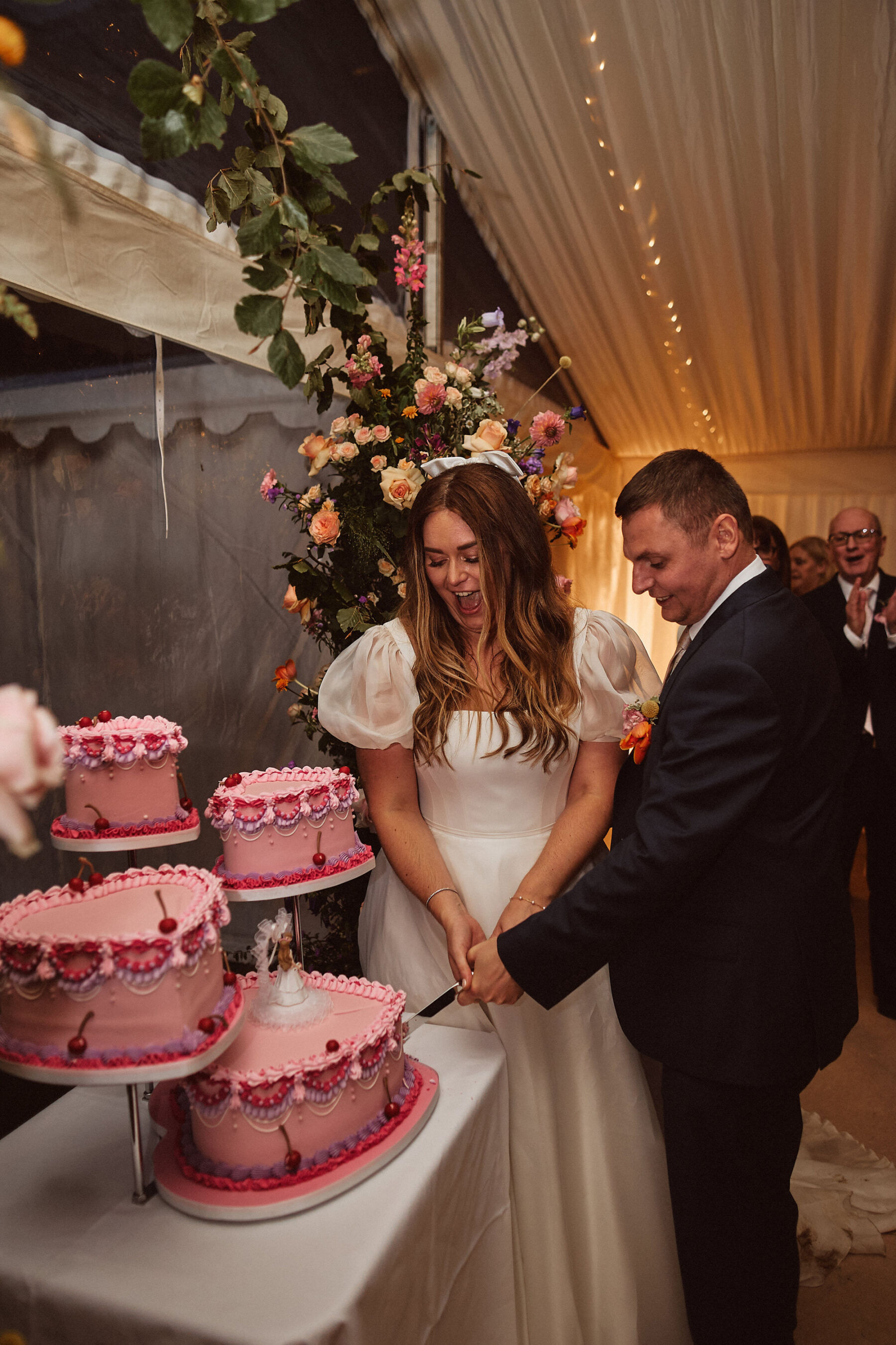 Bride and groom cutting the cake. There are 4 pink, heart shaped cakes with frilly retro style icing.