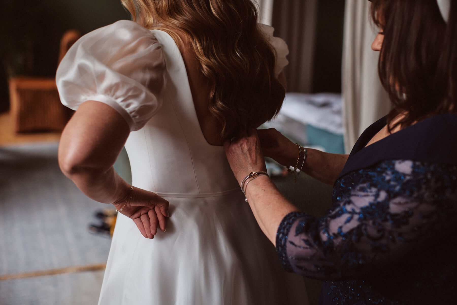 Mother of the bride buttoning her daughter into her Suzanne Neville wedding dress.