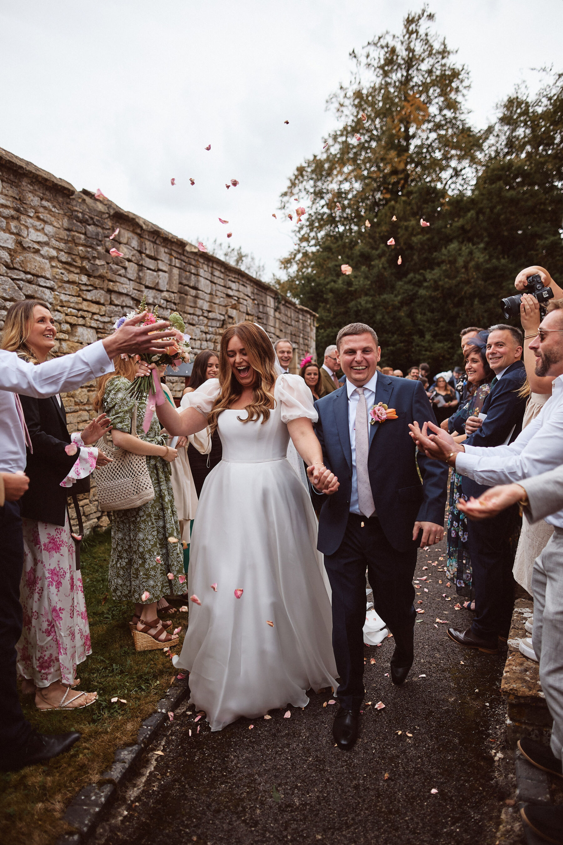 Bride and groom exiting in a flurry of confetti. The bride wears a puff sleeve Suzanne Neville wedding dress from Miss Bush Bridal boutique.