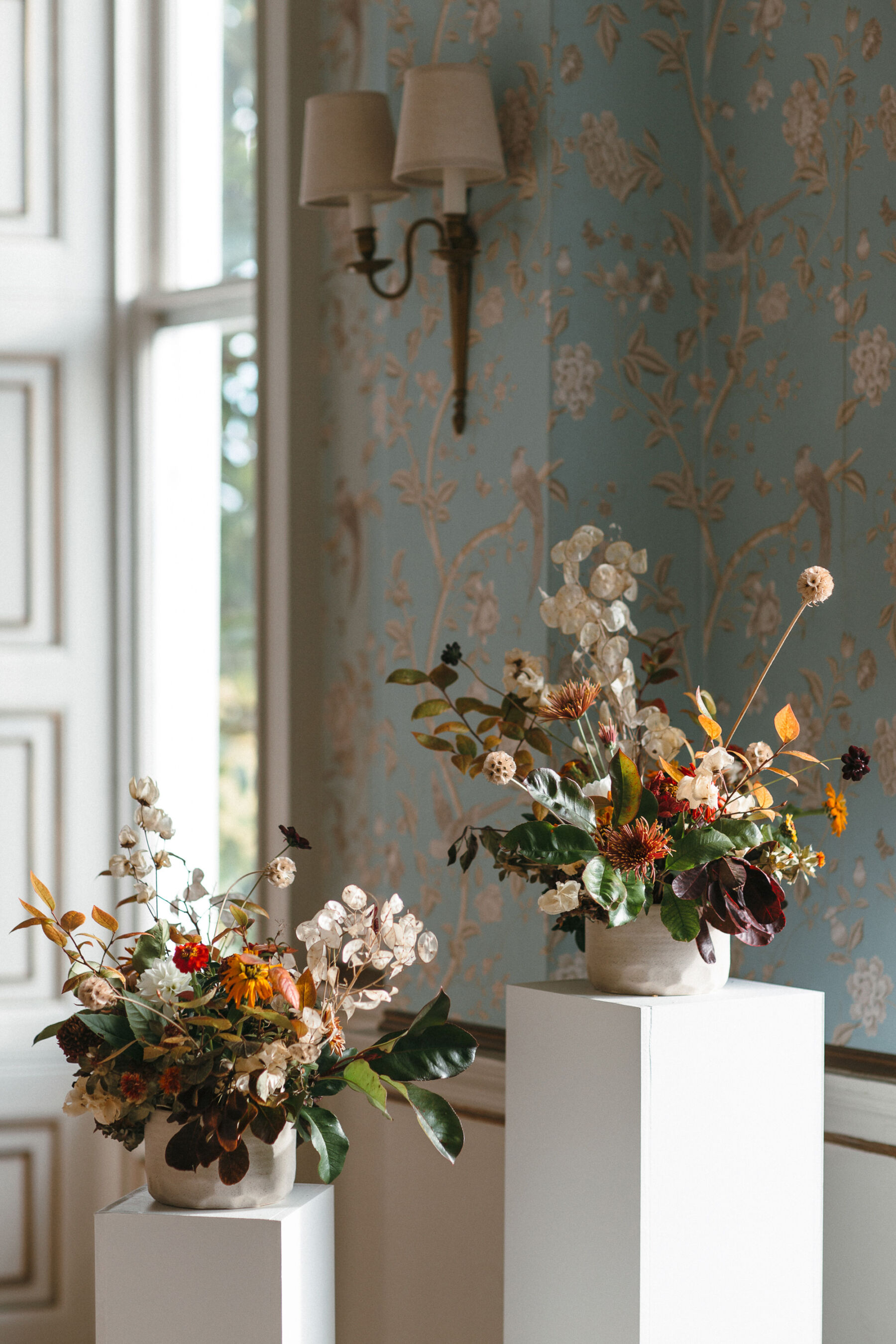 Two white columns with a bowl of Autumn wedding flowers on the top.