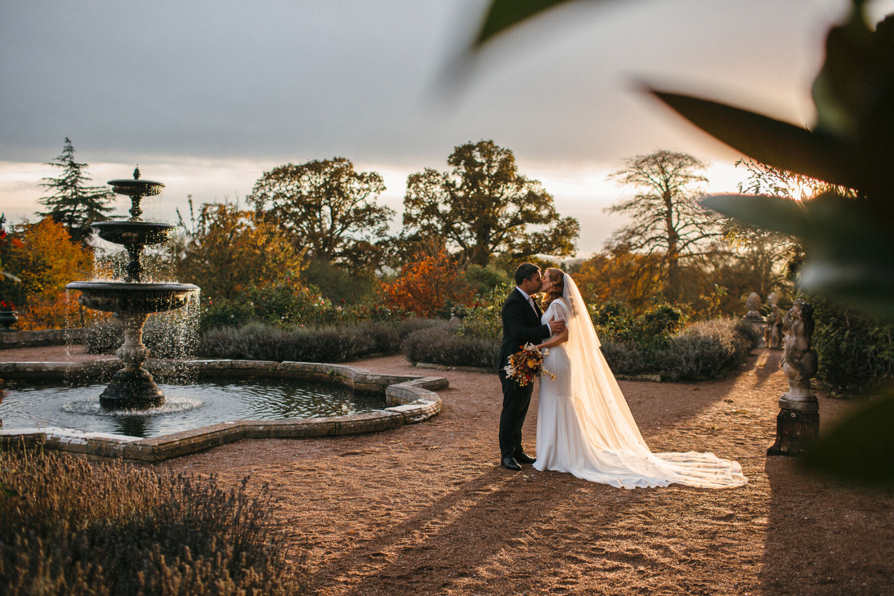Romantic golden hour shot of a bride and groom standing by an ornamental pond in the grounds of Pynes House in Devon. 