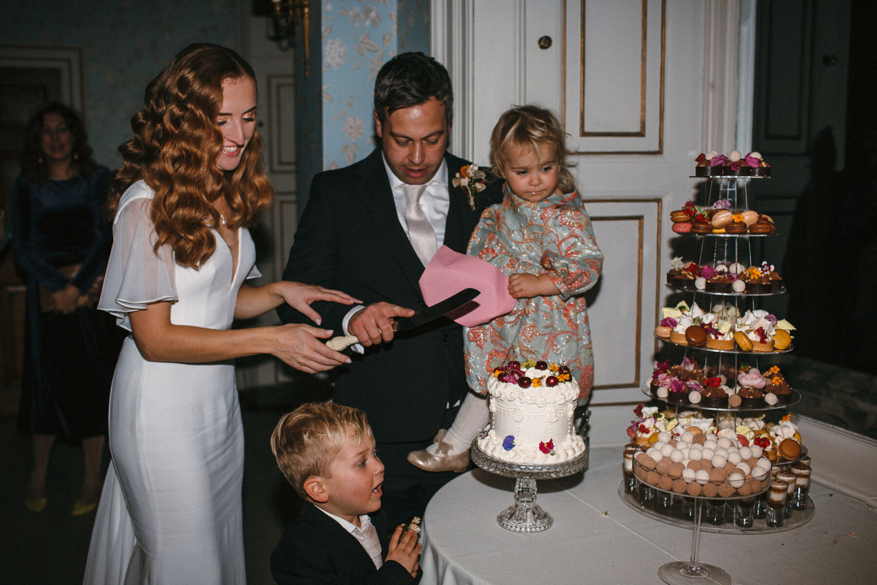 Bride and groom and their young children prepare to cut the cake, alongside a tower of sweet treats.