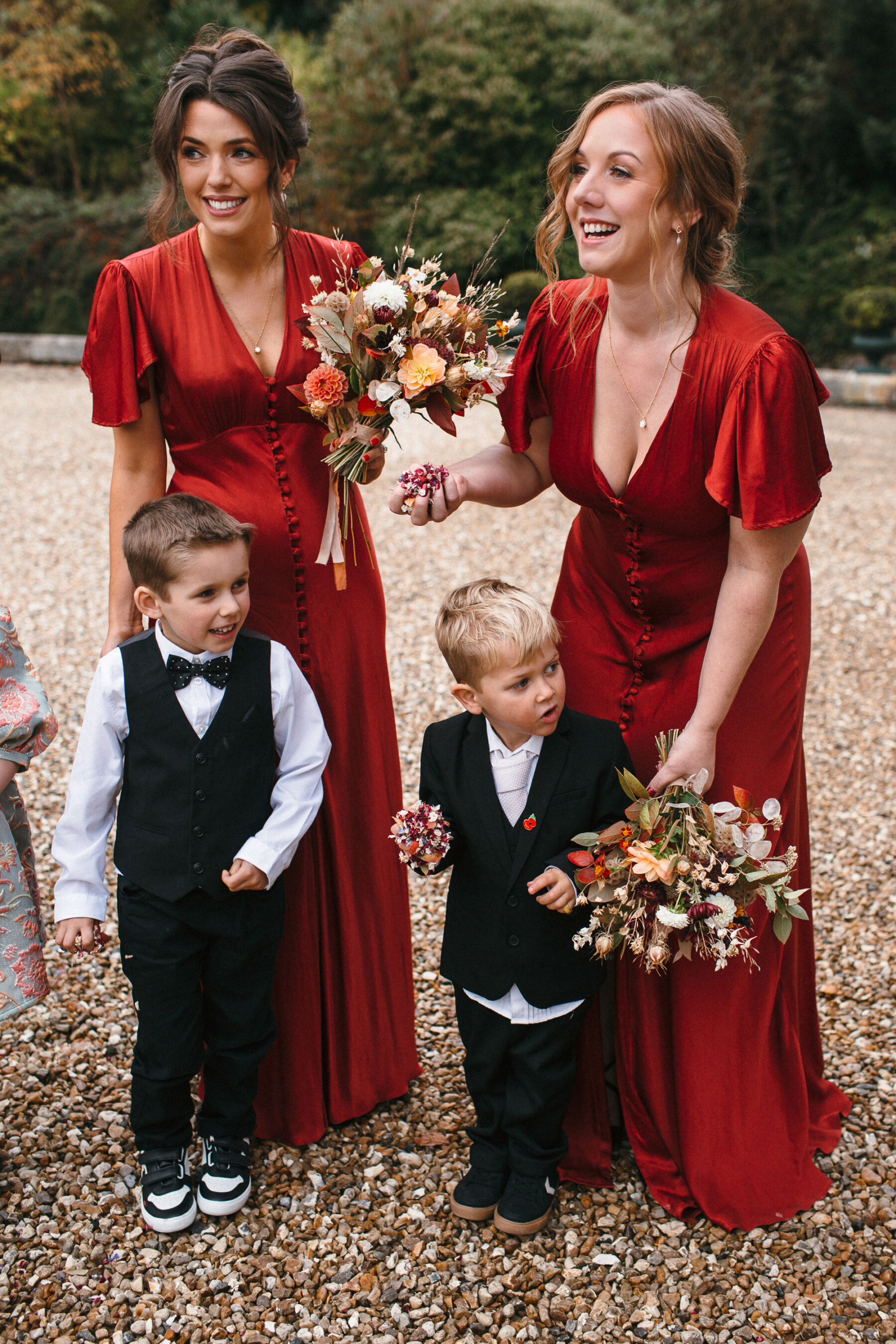 Bridesmaids in burned orange dresses from Ghost London. Page boys in littel suits with bow ties and waist coats. The bridesmaids carry Autumn wedding flowers.