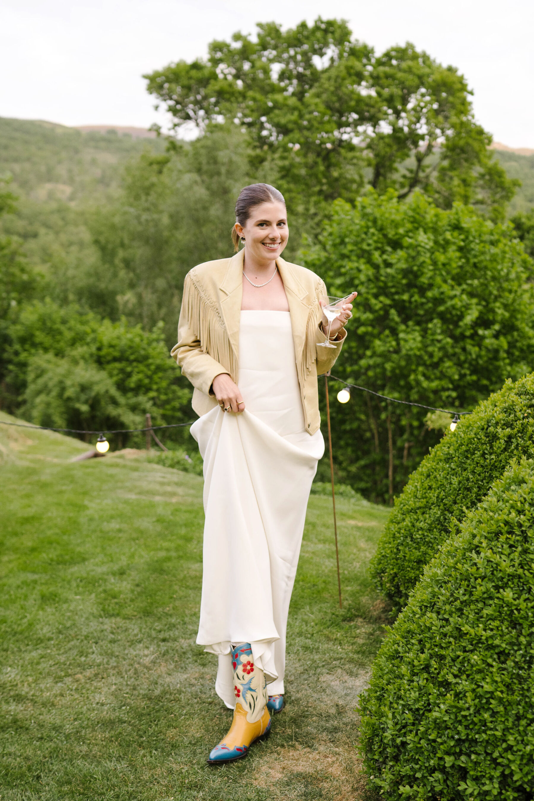 Bride in a tassel jacket, lifting her skirt gently to reveal a pair of cowboy boots. 