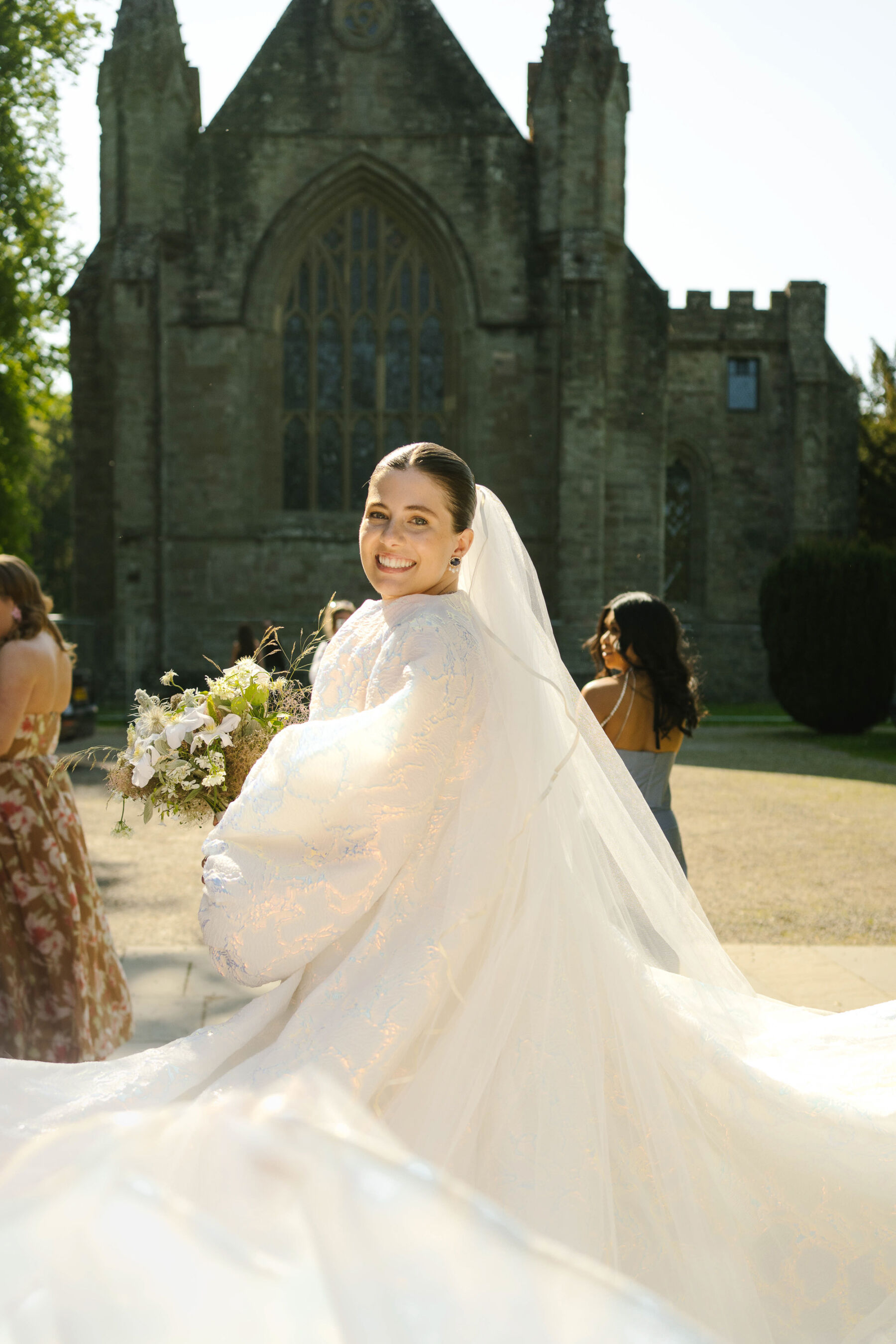 Bride wearing a billow sleeved Jesus Peiro coat and carrying a natural wedding bouquet by Joseph Massie.