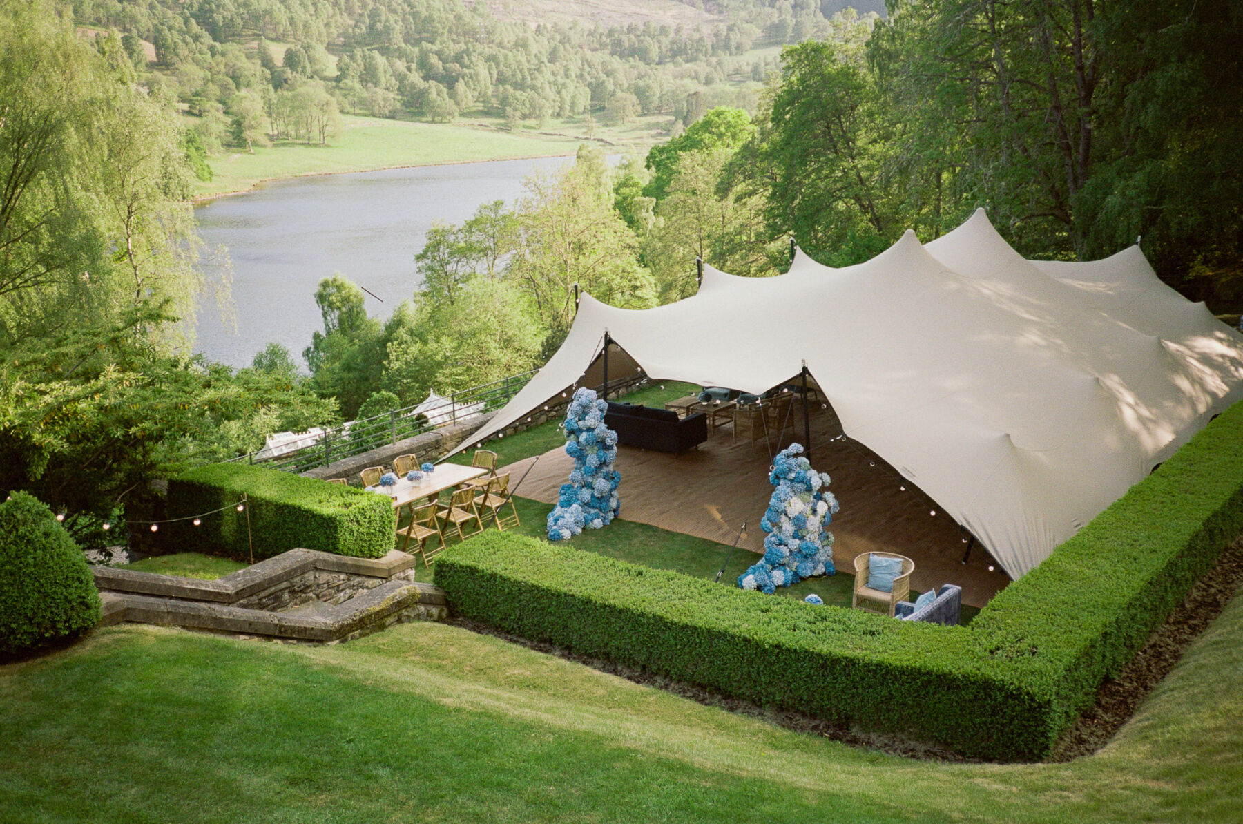 Marquee in the grounds of a Scottish castle overlooking a river. The marquee entrance is decorated with towers of blue and white hydrangea by Joseph Massie.