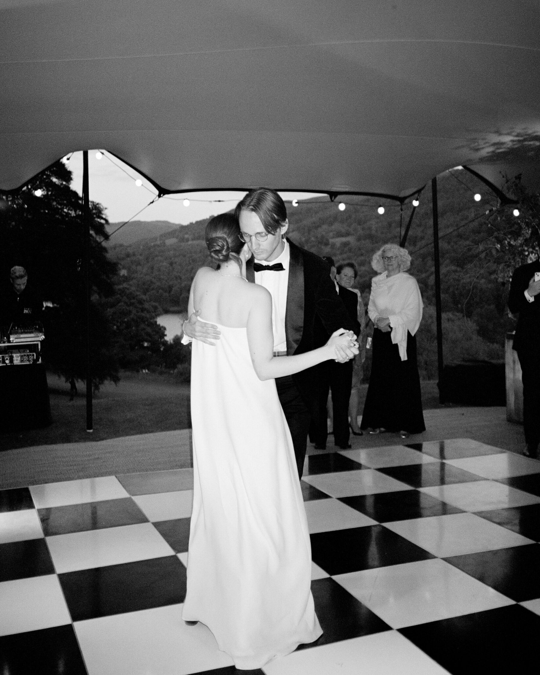 Bride with a low bun, wearing a wedding dress by The Row and dancing in the embrace of her groom. The First Dance.