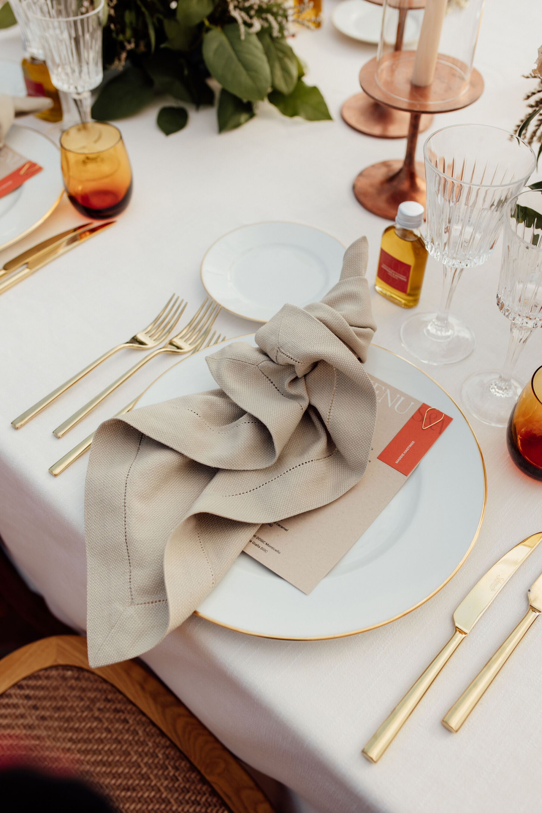 Pale linen napkins and modern wedding stationery placed on a china plate with gold rim, and gold cutlery, for a modern Italian wedding. 