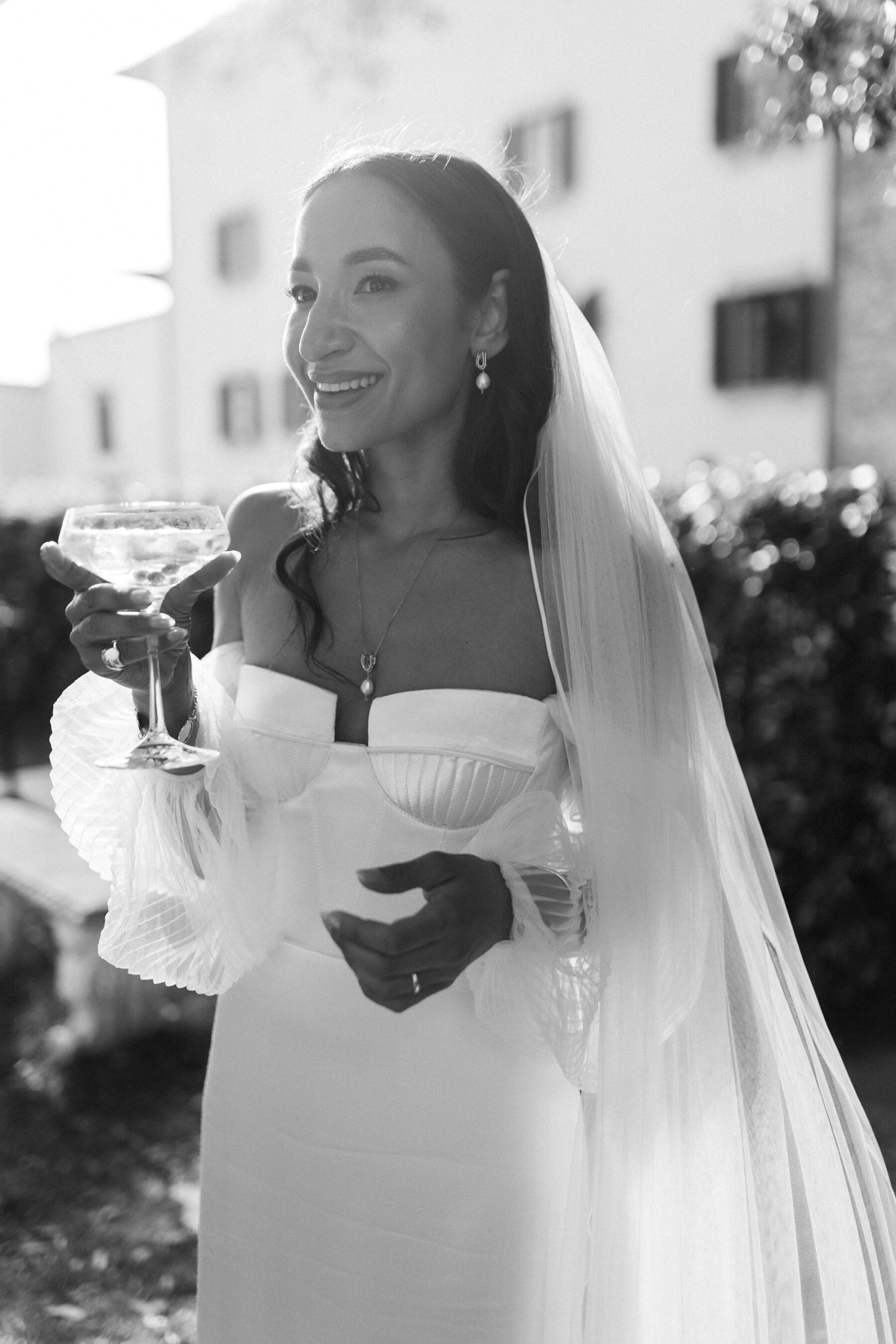 Bride wearing an Alena Leena wedding dress raises a glass of champagne as she enjoys her Italian wedding drinks reception. 