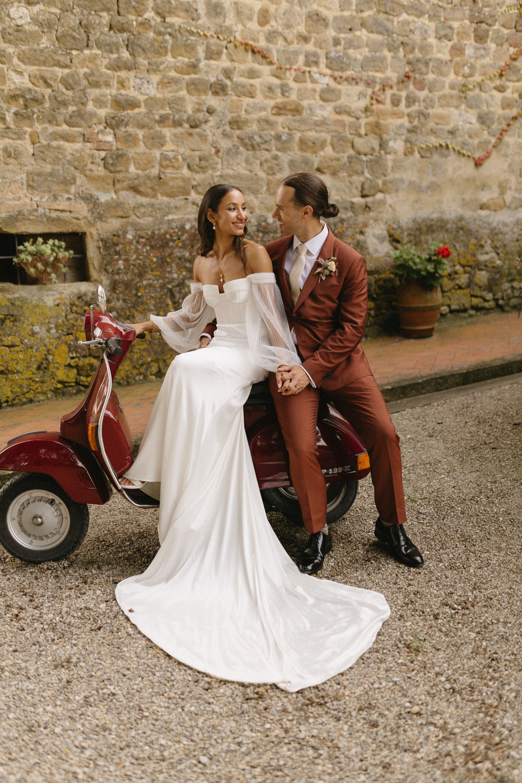 Bride sat on a vintage Vespa in Italy with her groom in an burned orange Paul Smith Suit. She wears an Alena Leena bridal gown with detachable tulle sleeves.