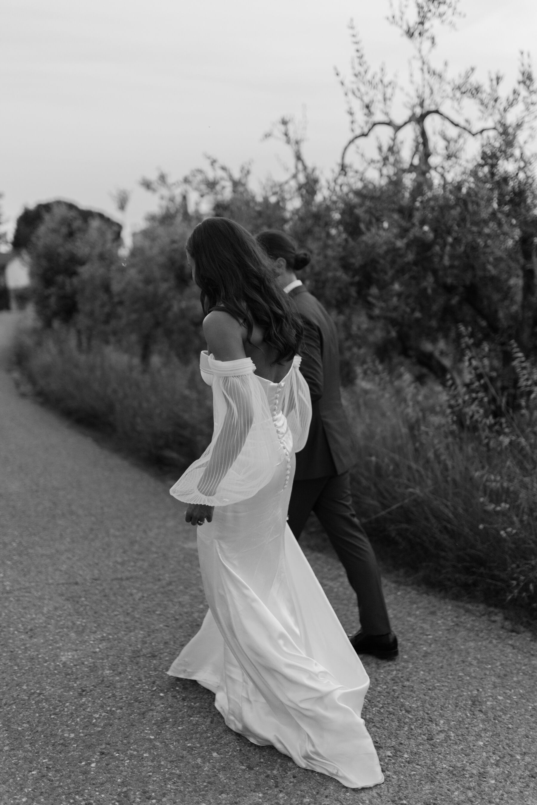 Black and white photograph of a modern bride in her strapless, Alena Leena bridal gown, walking with her groom just out of shot. Mild blur on image.