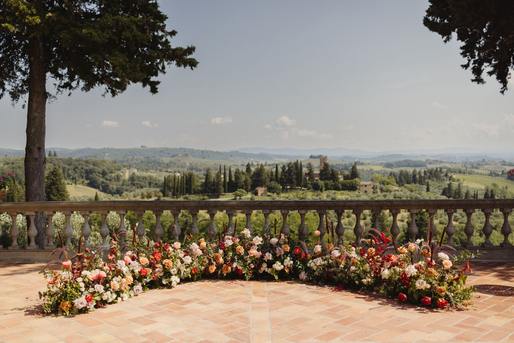 Curved flower installation on the ground, wedding ceremony backdrop. The flowers are for an Italian wedding and the scene features rolling hills of Tuscany in the backdrop.