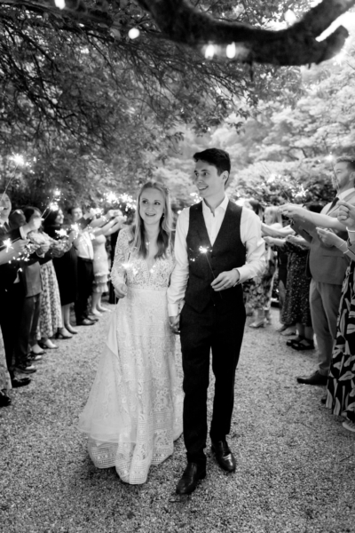 Happy bride and groom walking beneath trees with wedding sparklers