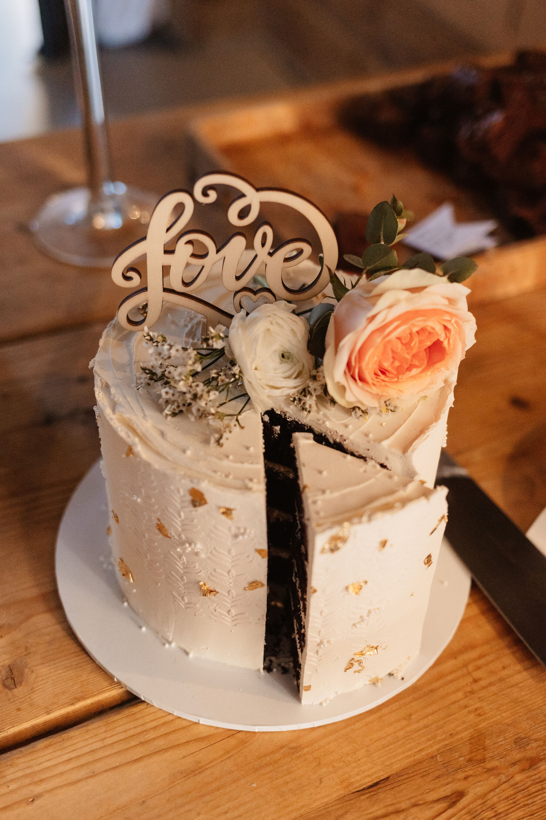 Single tier wedding cake topped with a wooden word 'Love' and a peach rose.