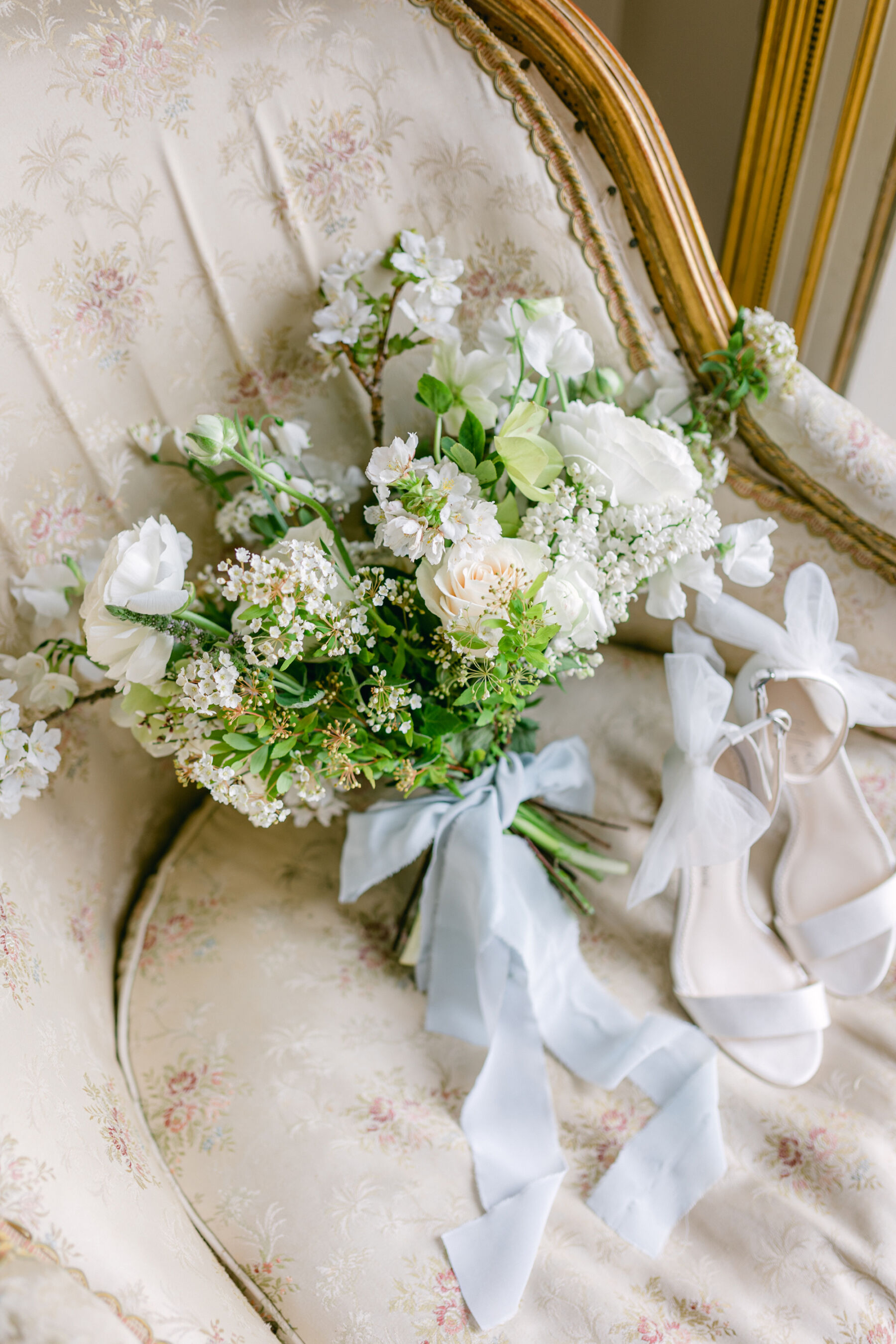 Elegant and romantic Spring bridal bouquet by Blue Sky Flowers. The bouquet is tied with a pale blue silk ribbon and comprises of all white flowers. Nearby is a pair of Bella Belle high heel open toe strappy bridal sandals, with a tulle ankle bow.