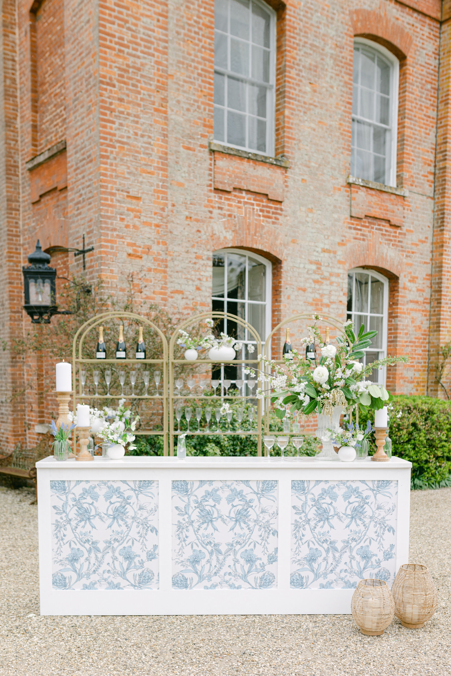 Elegant mobile wedding bar, with pattern blue decor, white wedding flowers and brass shelves for the bottles and glasses. White wedding flowers decorate the bar. Avington Park wedding venue,  Hampshire.