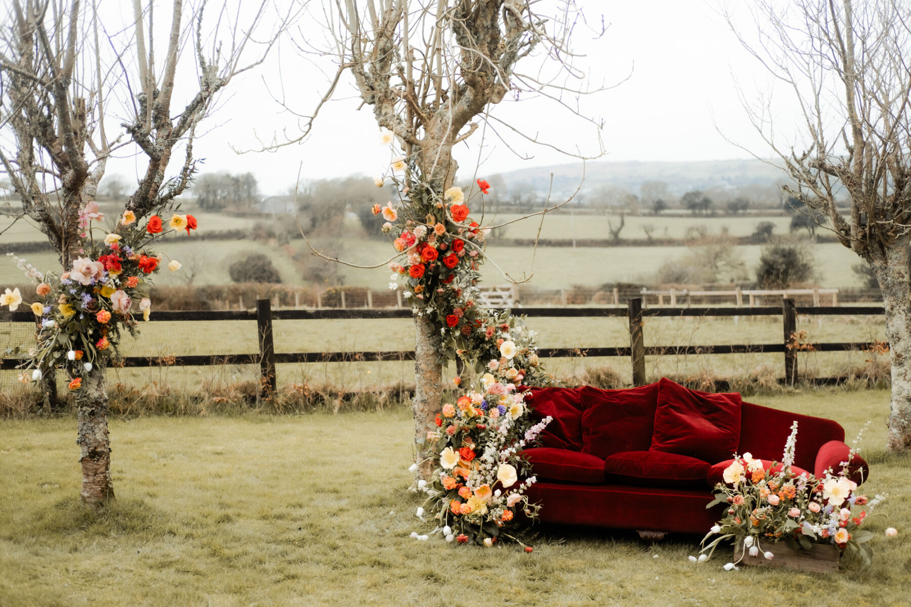 The Cornish Place wedding venue in Cornwall. Outdoor wedding location in a field with a plush red velvet sofa and modern country wedding flowers.