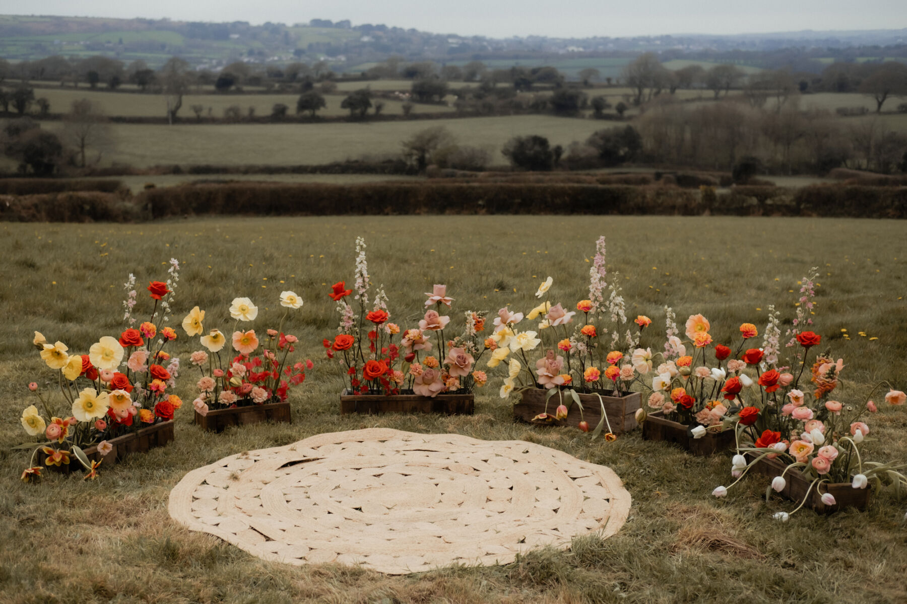 Meadow flowers in boxes for an outdoor wedding, positioned in a semi-circle with a bohemian rug. The Cornish Place wedding venue, Cornwall.