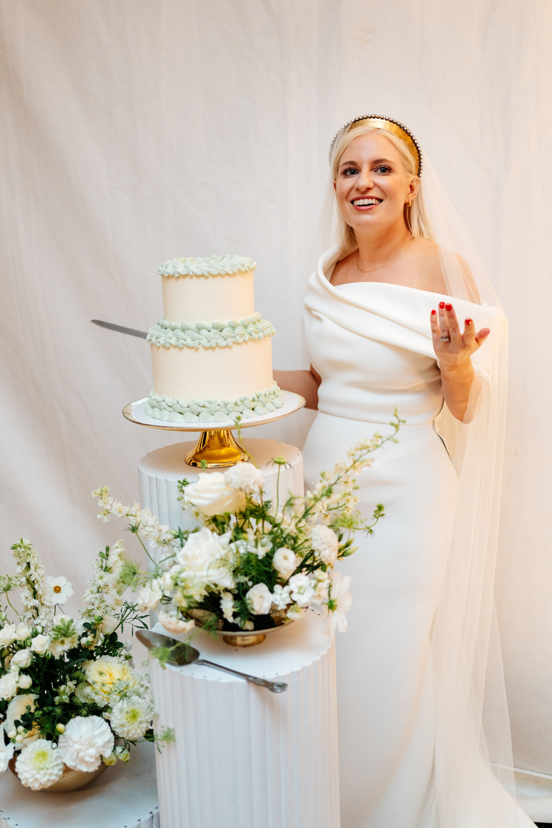Modern bride in a Toni Maticevski wedding dress holding a knife to cut her simple two tier wedding cake which has pale green frilly icing around the base.