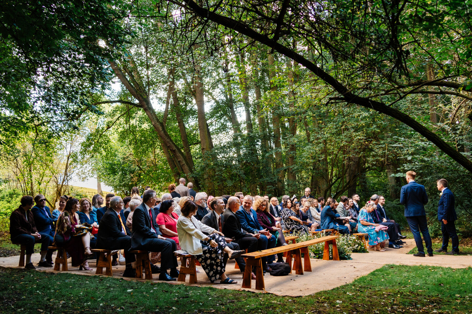 Wedding guests seated on benches for an outdoor woodland ceremony.