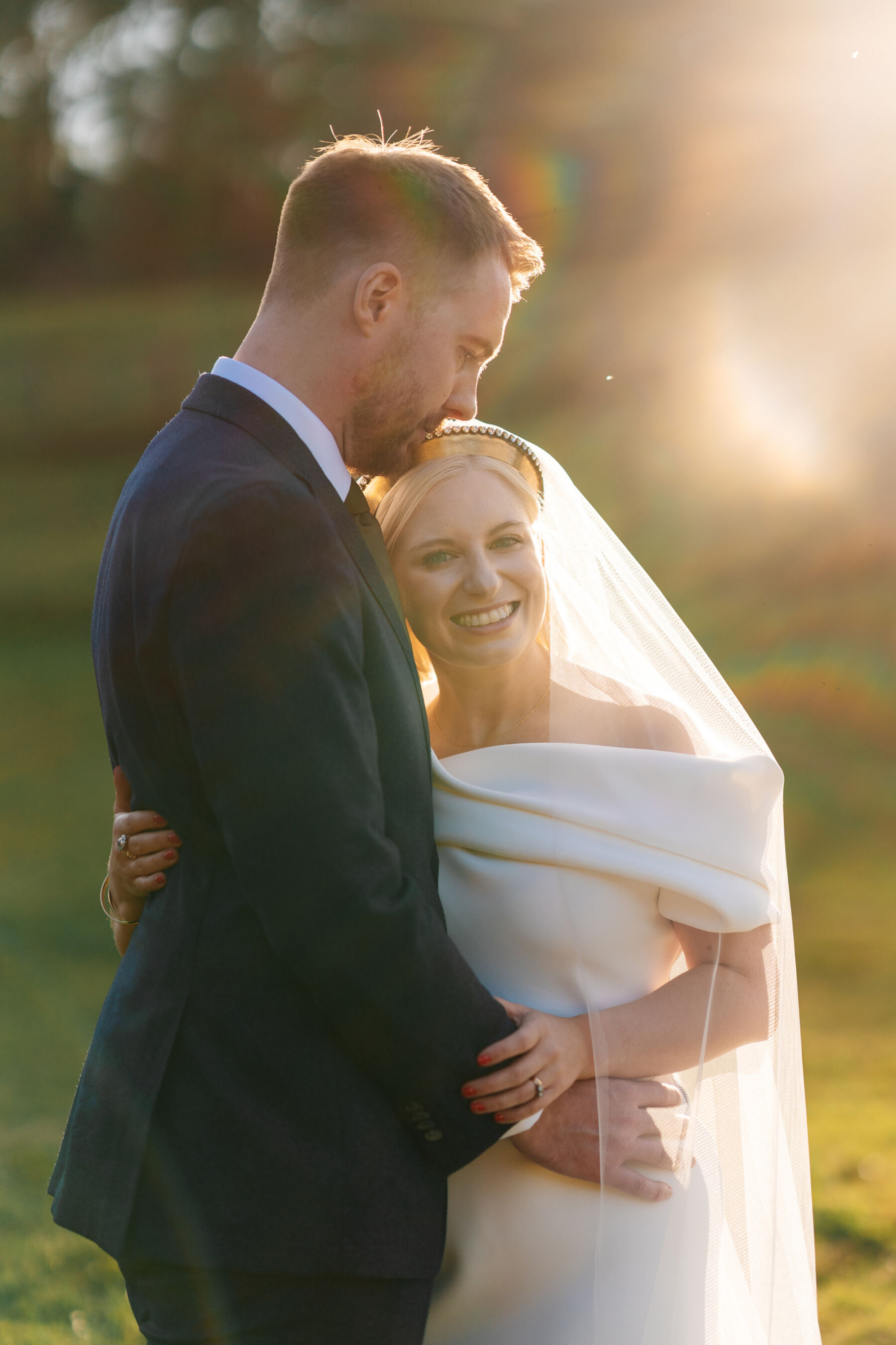 Golden hour shot of modern bride wearing a Toni Maticevski wedding dress as she is embraced by her groom.