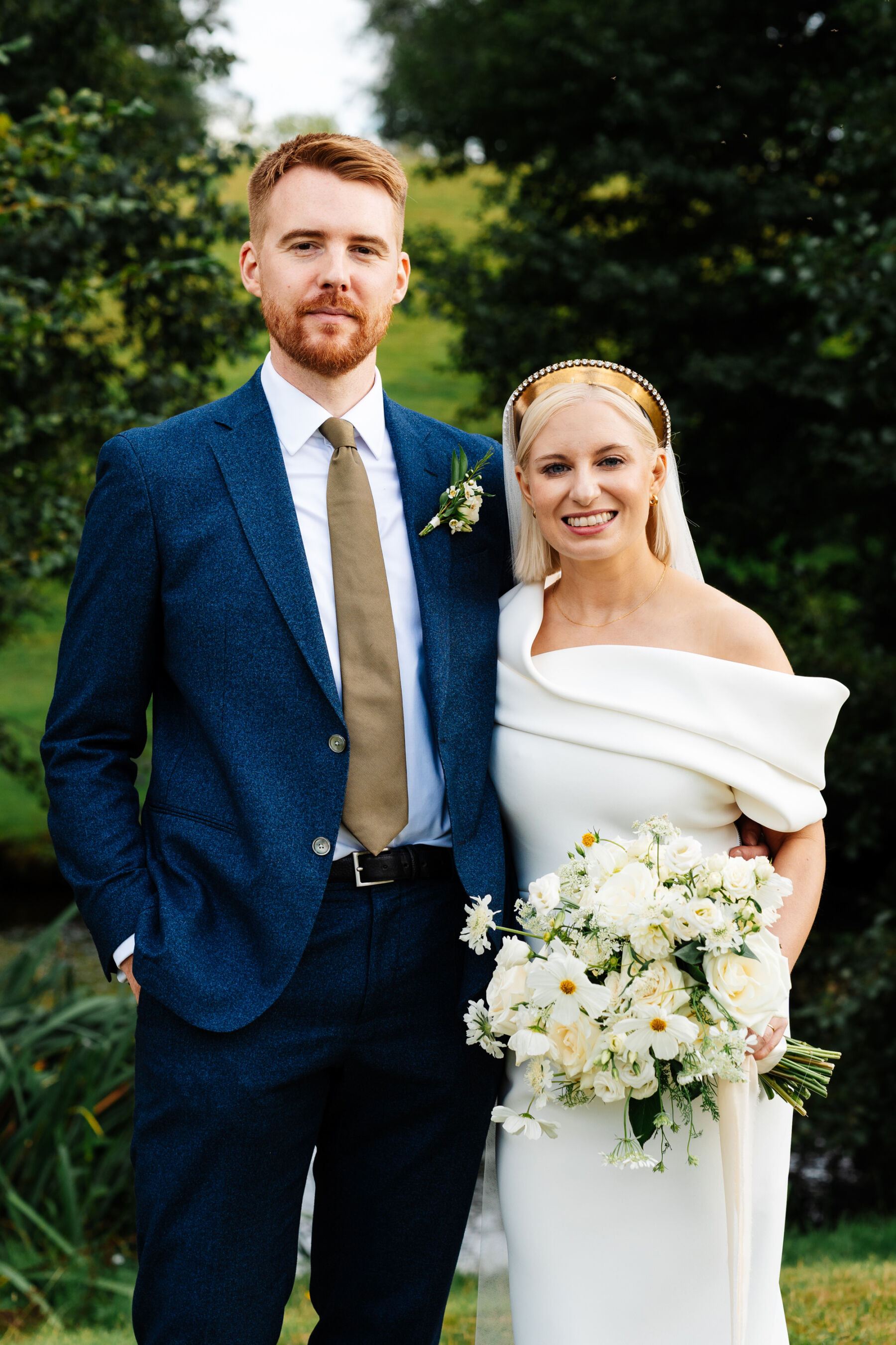 Modern bride wearing a Toni Maticevski wedding dress and golden headpiece. Groom in blue suit and olive green tie.