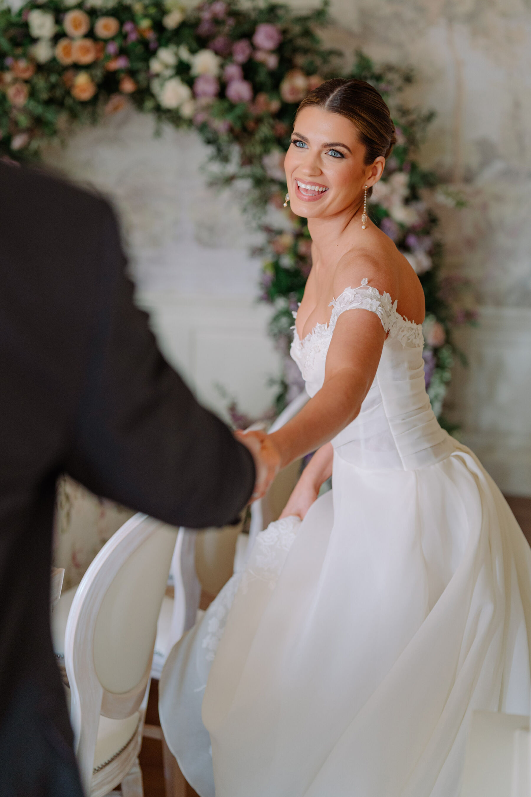 Joyful movement shot of model bride wearing an elegant and feminine off the shoulder bridal gown by Josephine Scott London. Kamila Nowak Photography.