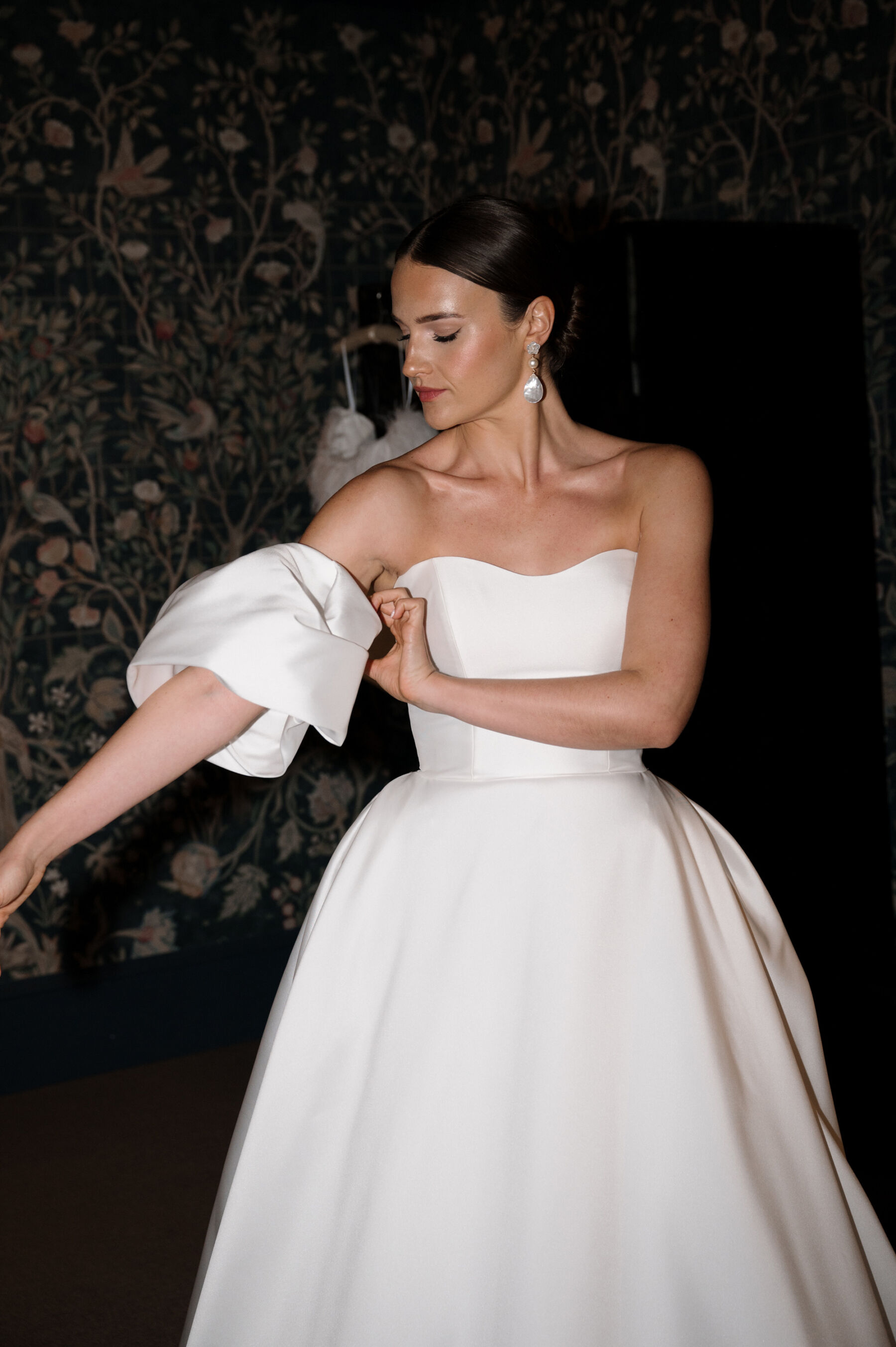 An Elegant Black Tie Wedding at Hampton Manor in Birmingham, with a Badgley Mischka Gown 25 Bride wearing a Badgley Mischka wedding dress with removable puff sleeves. She carries a white wedding bouquet and wears long pearl earrings. Taylor Hughes Photography.