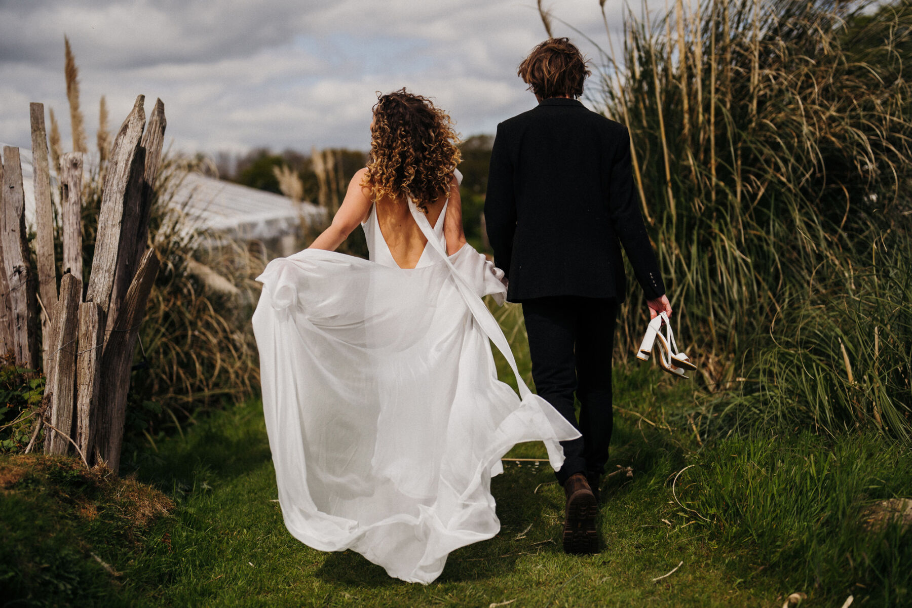 Bohemian bride wiht her dress wafting behind her as she walks through grasses at Wonderland Sussex. Voyteck Photography.