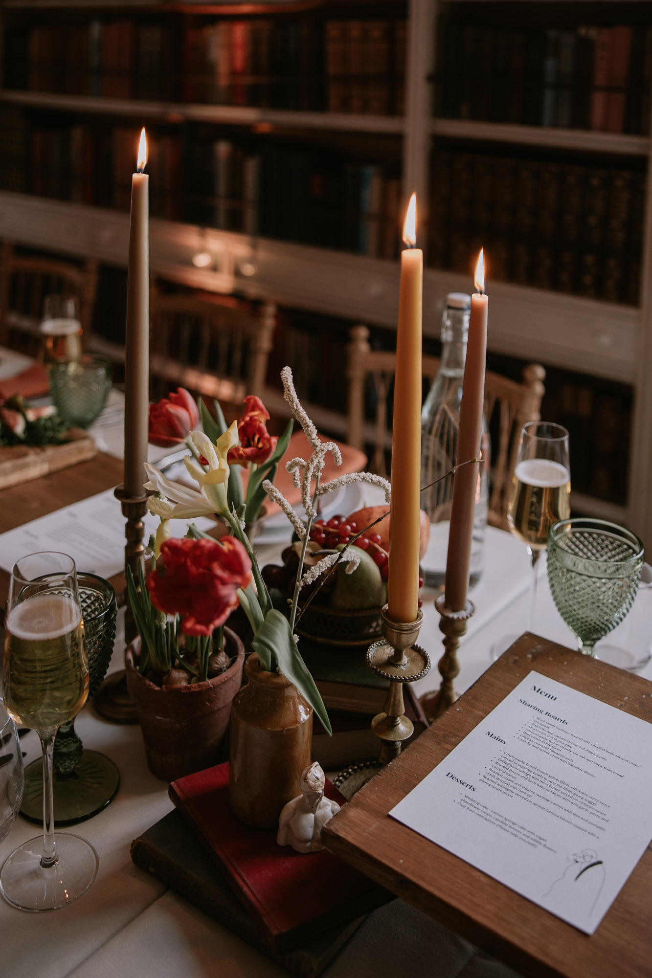 Tall taper candles in peach and orange shades. Green cut glass and small pots of flowers. Wedding table decor. Marta Ilardo Photography 