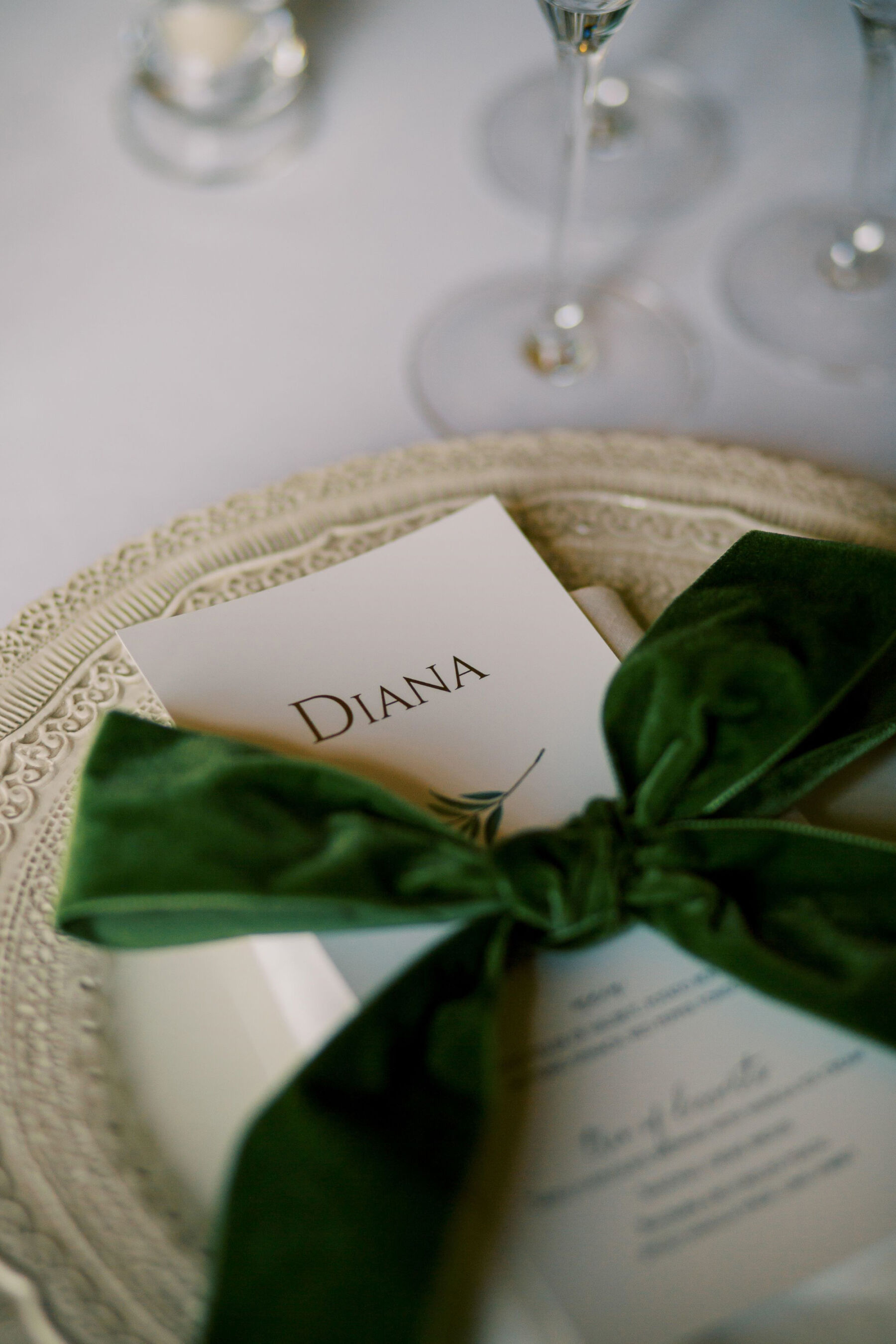 Gothic Architecture Inspired Wedding Styling, at Strawberry Hill House 16 Dark green velvet bow positioned on a table setting. The bow is created by the Embroidered Napkin Company. The bow sits up top of elegant wedding stationery wtih the guests name and a menu. Helen Warner Photography.