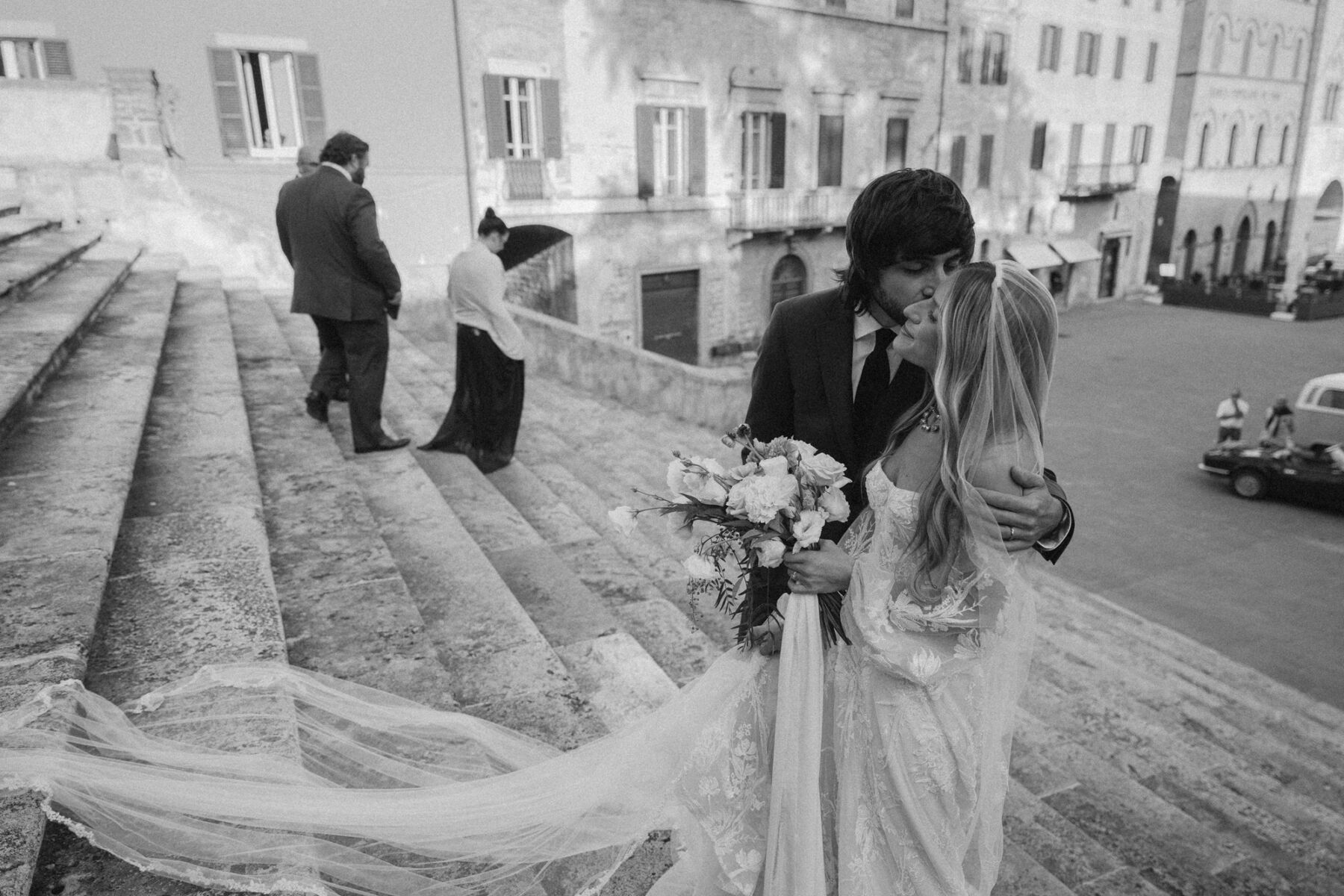 Mikaela in Alena Leena For Her Elegant Italian Wedding at Villa Fattoria di Vibio 35 Tender black and white photography of groom embracing and kissing his bride on the steps outside an Italian church in Umbria. Photography by Stefano Santucci.