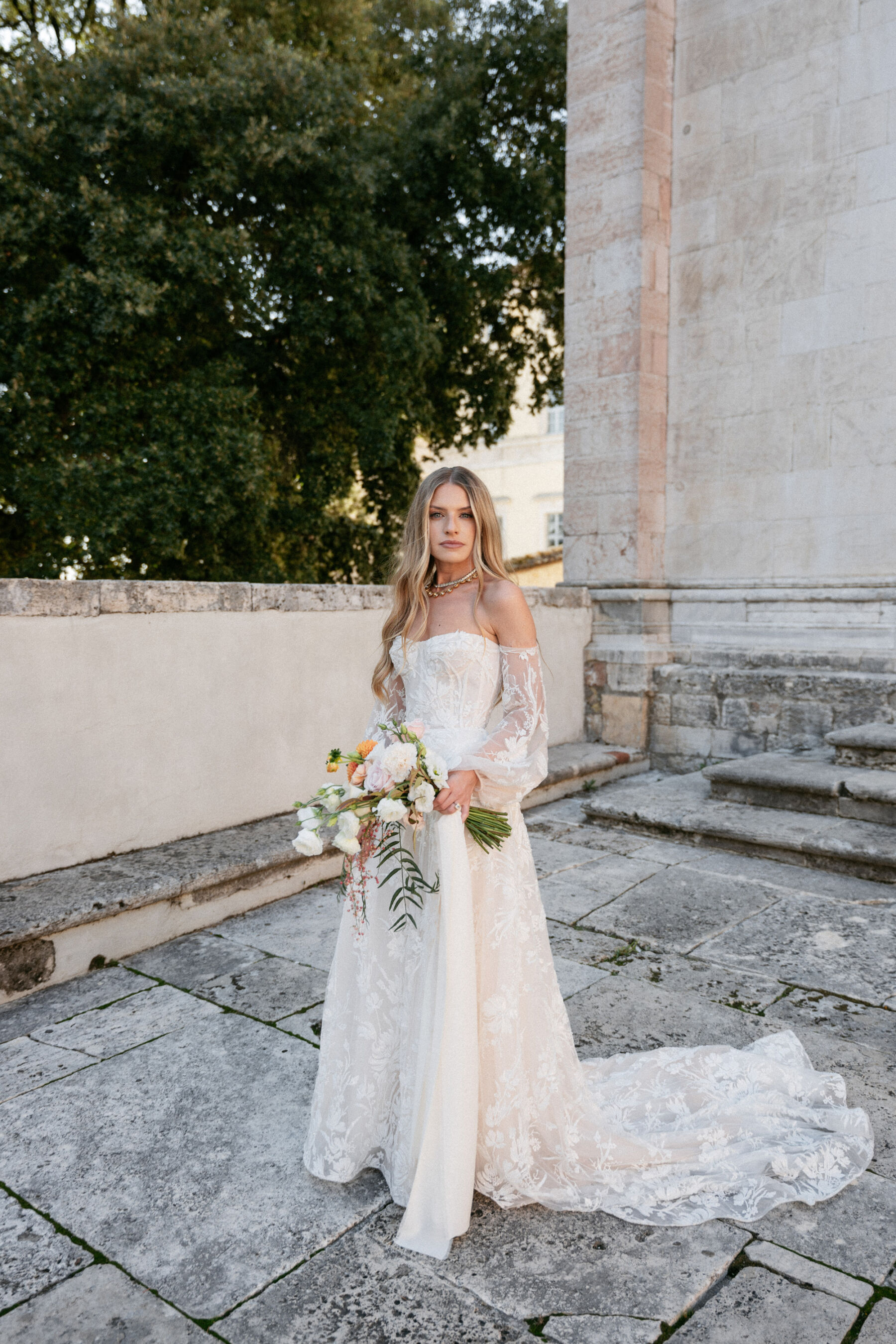 Mikaela in Alena Leena For Her Elegant Italian Wedding at Villa Fattoria di Vibio 37 Bride with long blonde wavy hair wearing an Alena Leena wedding dress with removable sleeves and carrying a bright medium sized summer wedding bouquet. Photography by Stefano Santucci.