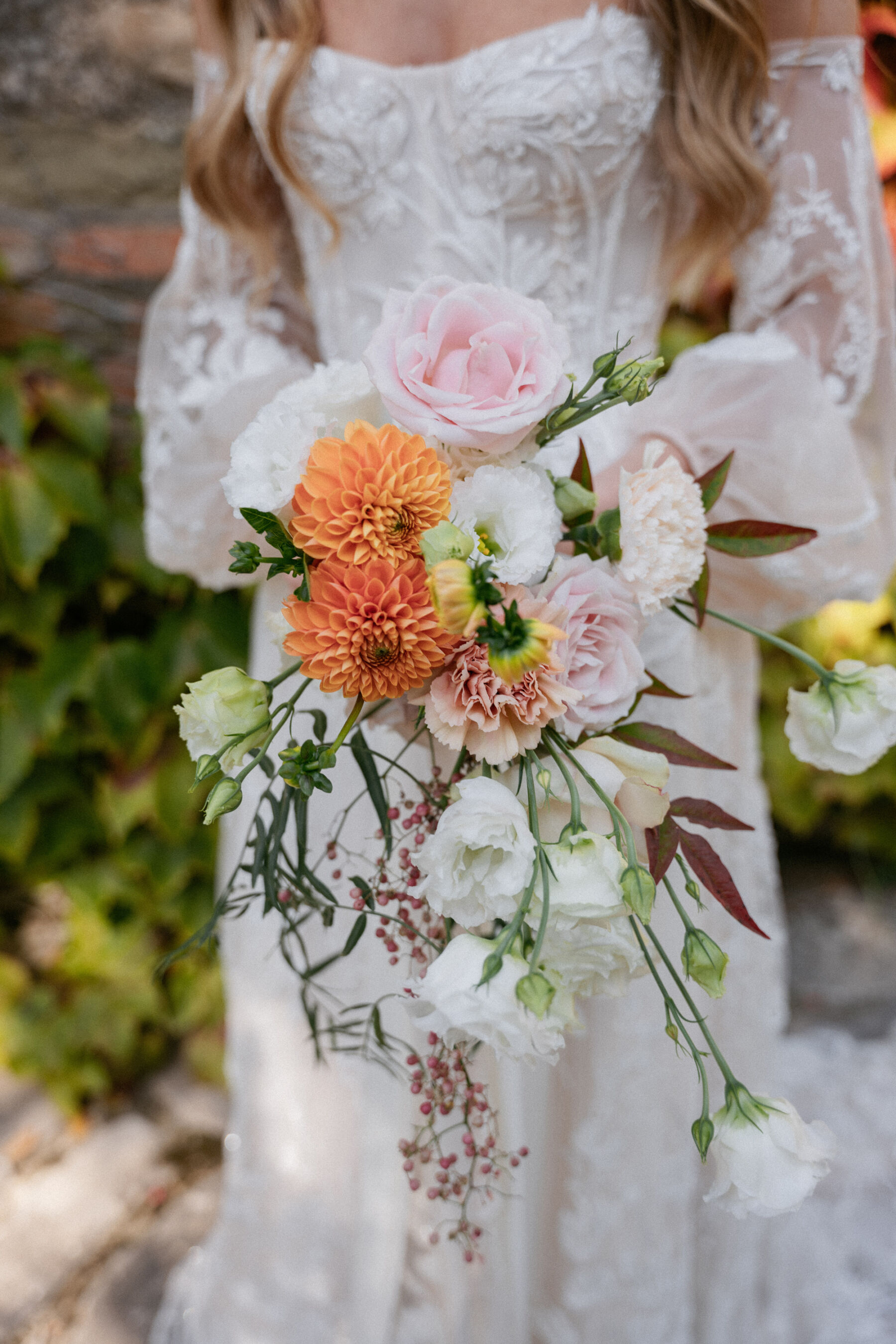 Mikaela in Alena Leena For Her Elegant Italian Wedding at Villa Fattoria di Vibio 17 Close up photograph of a long, loose bridal bouquet with orange Dahlia and pale pink roses. Photography by Stefano Santucci.