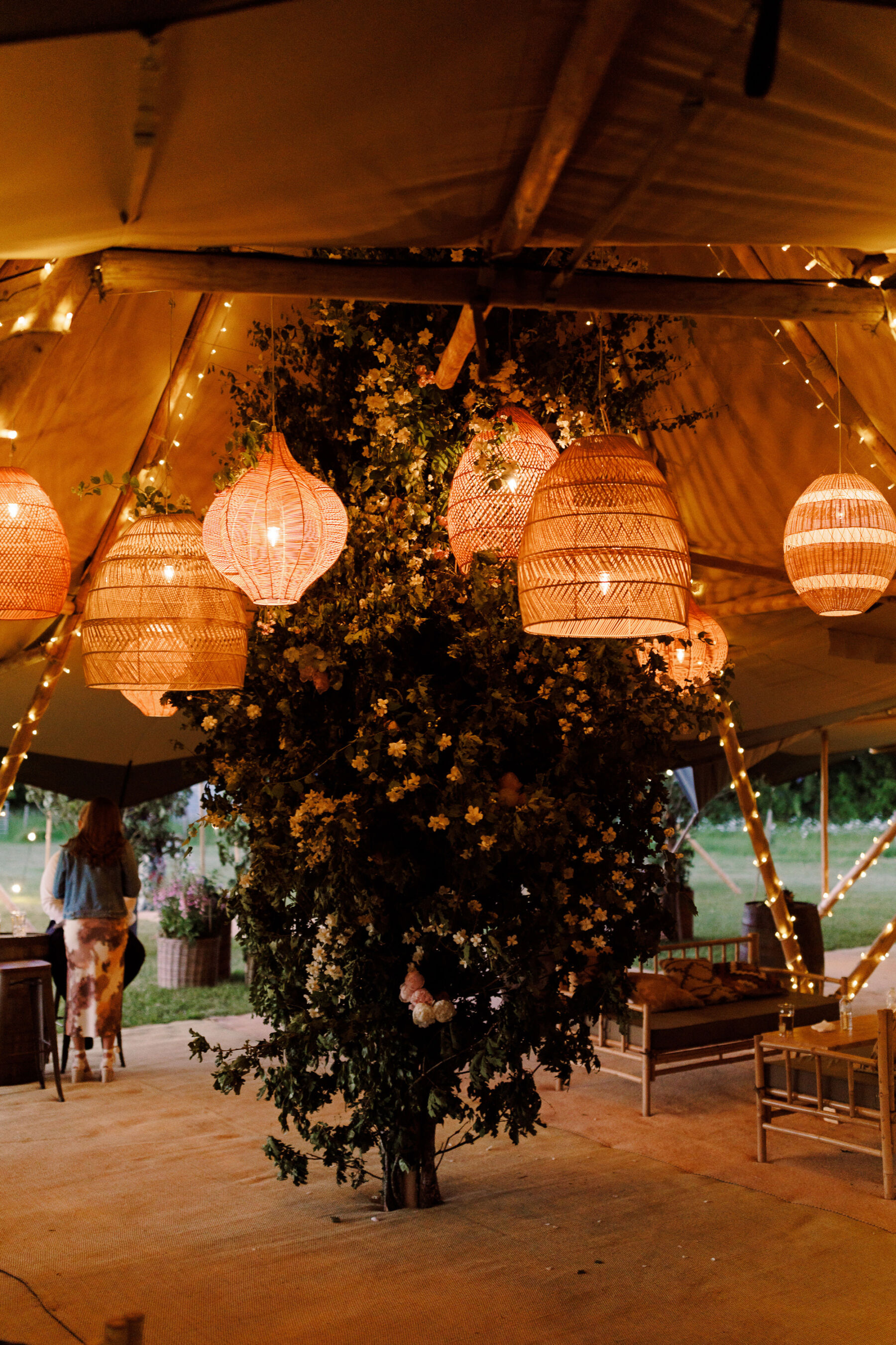 Wedding tipi with whicker light shades hanging from wooden bars and fairy lights decorating the poles.