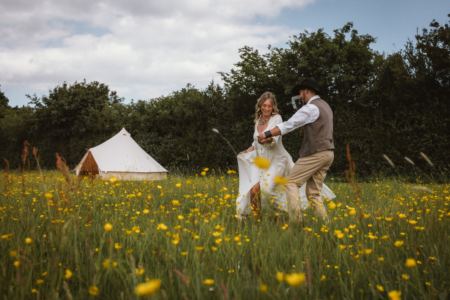 Wickerwood Farm, an Eco Friendly, Glamping Wedding Venue in East Sussex 19 Bride and groom running through a field of buttercups at Wickerwood Farm wedding venue, East Sussex.
