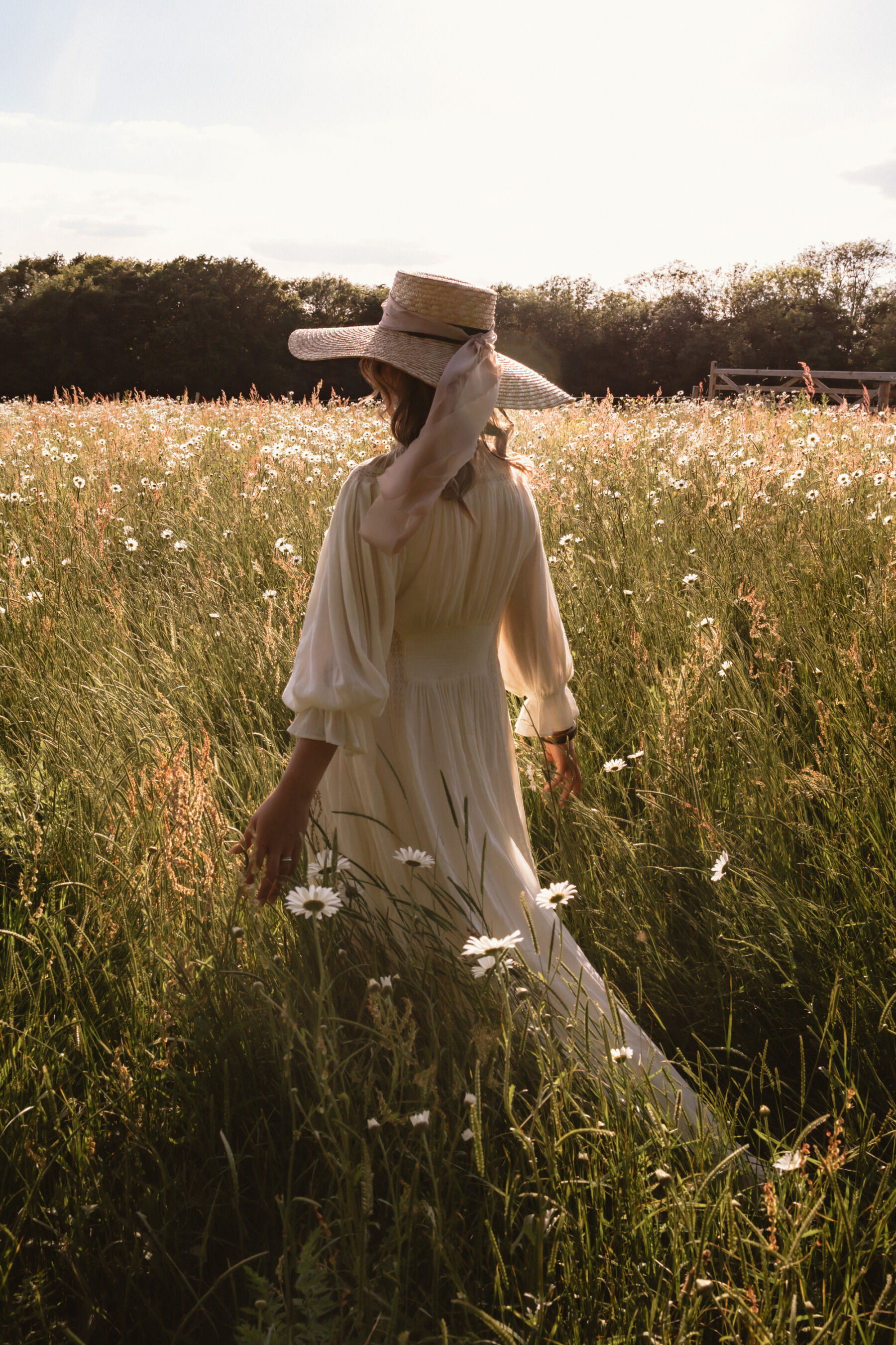 Wickerwood Farm, an Eco Friendly, Glamping Wedding Venue in East Sussex 33 Bride in a pretty straw hat with a silk ribbon and a Free People Dress wanding through a field full of wildflowers during golden hour at Wickerwood Farm wedding venue, East Sussex.