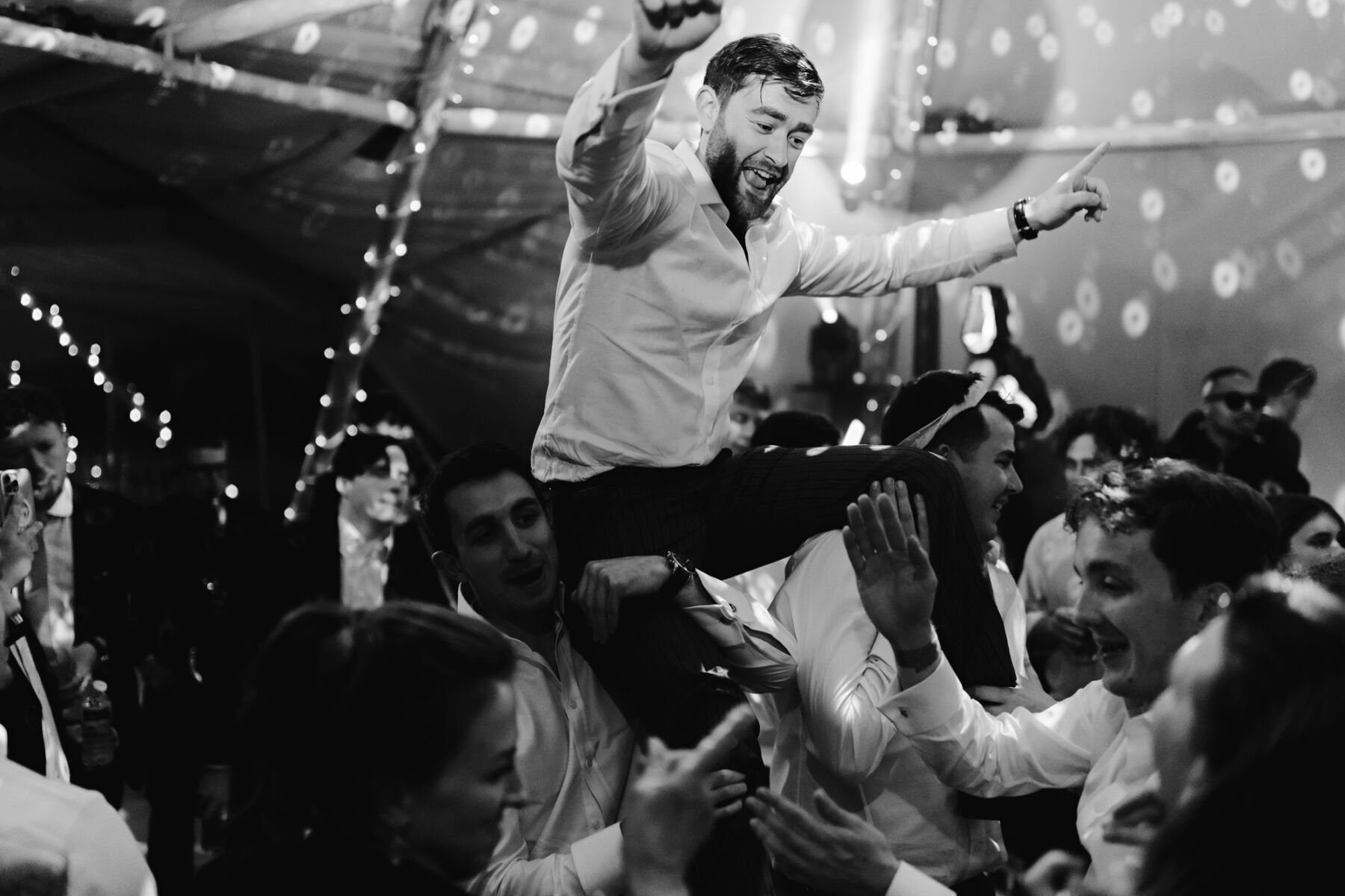 Groom being lifted into the air by wedding guests and revellers on his wedding day inside the tipi.
