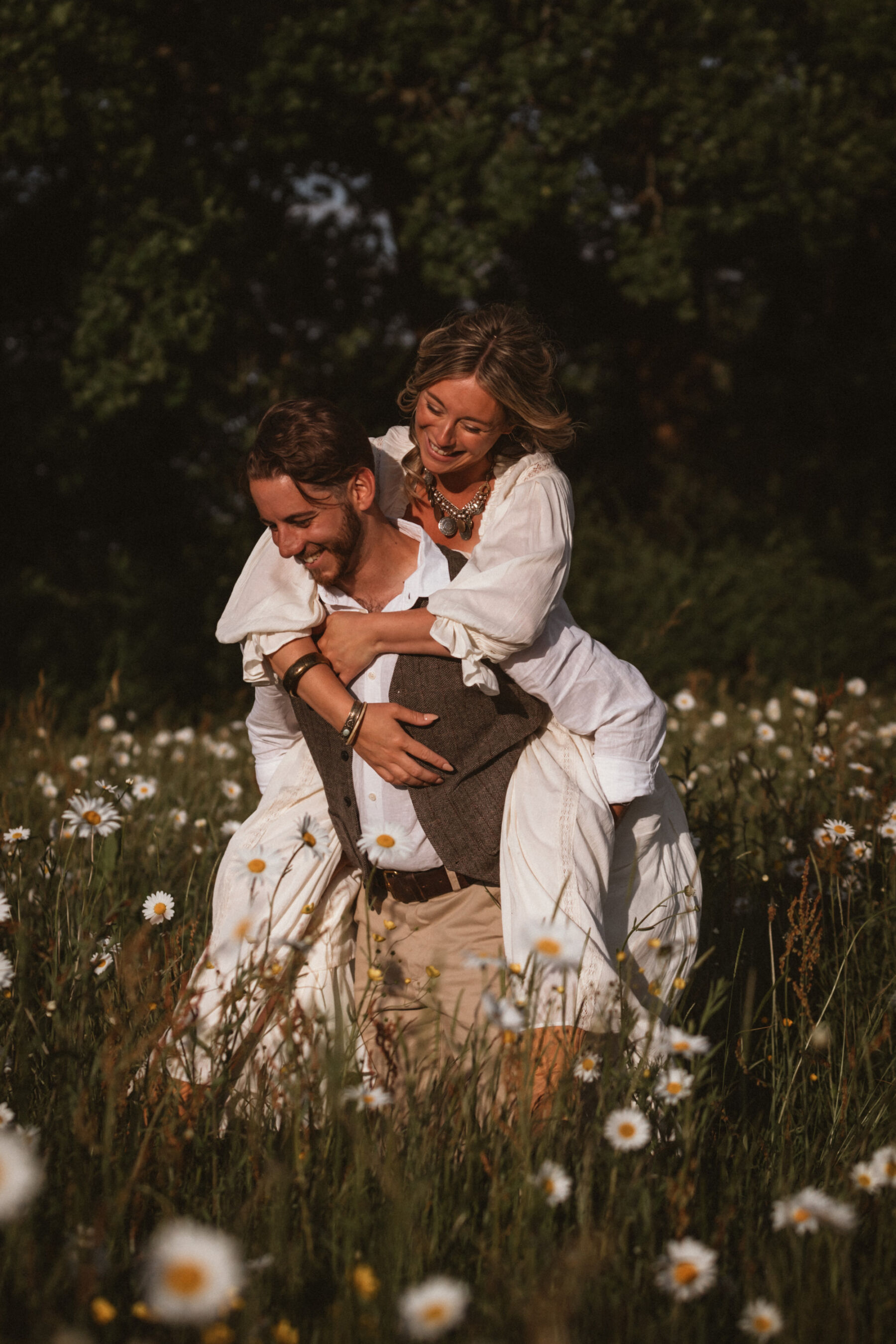 Wickerwood Farm, an Eco Friendly, Glamping Wedding Venue in East Sussex 15 Groom with bride on his back as they have a playful moment inside a field full of flowers during golden hour at Wickerwood Farm wedding venue, East Sussex.