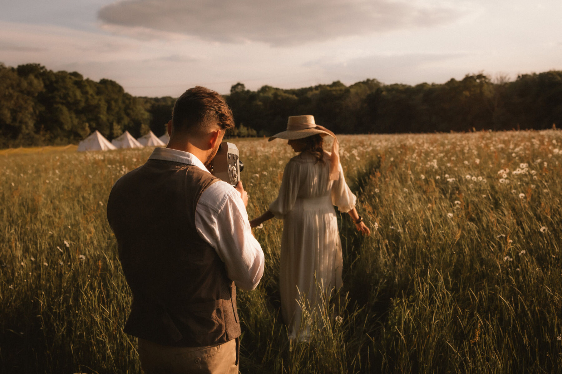 Wickerwood Farm, an Eco Friendly, Glamping Wedding Venue in East Sussex 25 Bride and groom wandering through a wildflower meadow at golden hour, towards a collection of bell tents at Wickerwood Farm wedding venue, East Sussex.