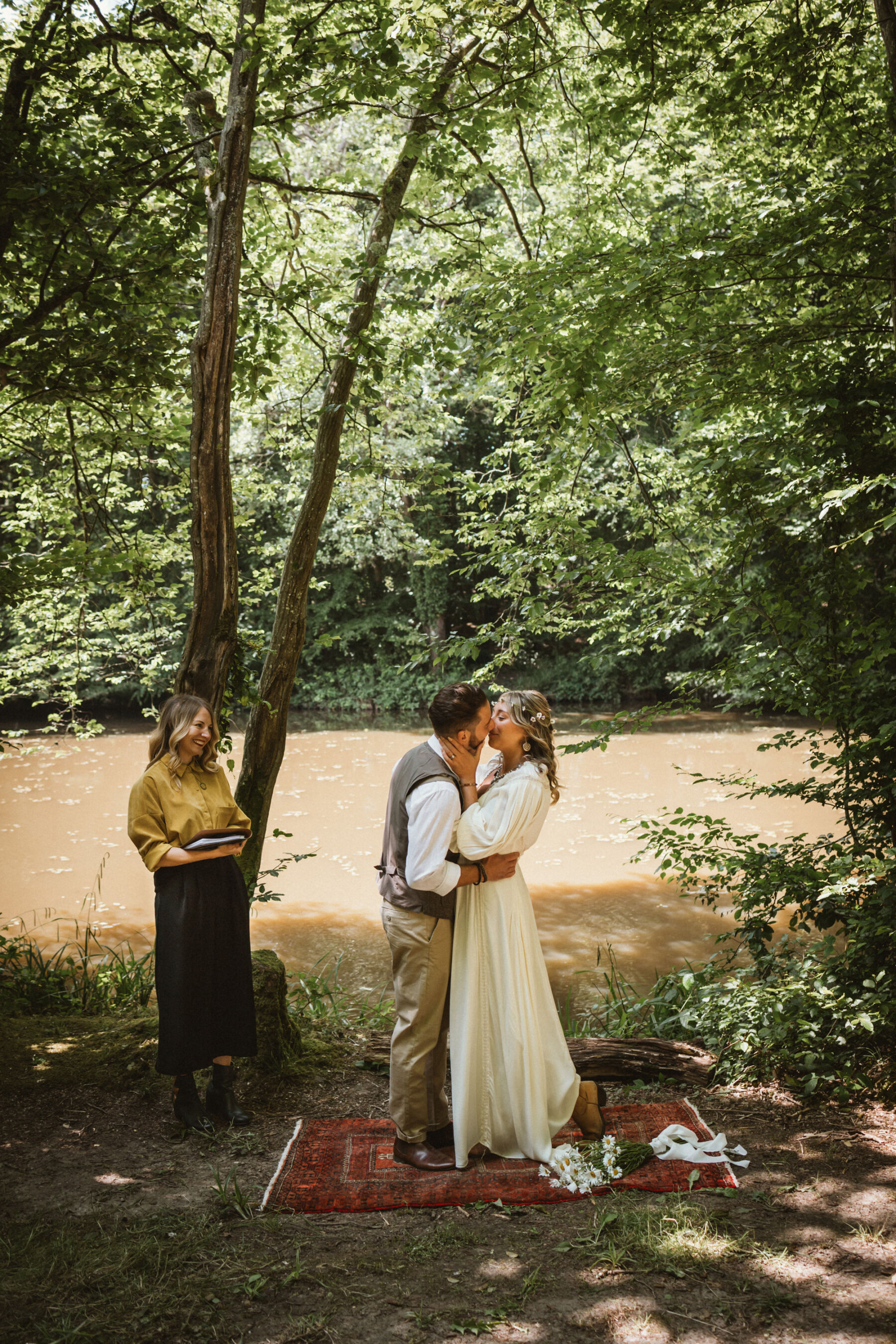 Wickerwood Farm, an Eco Friendly, Glamping Wedding Venue in East Sussex 11 Bride and groom kissing at the end of the wedding ceremony by the river at Wickerwood Farm wedding venue, East Sussex.