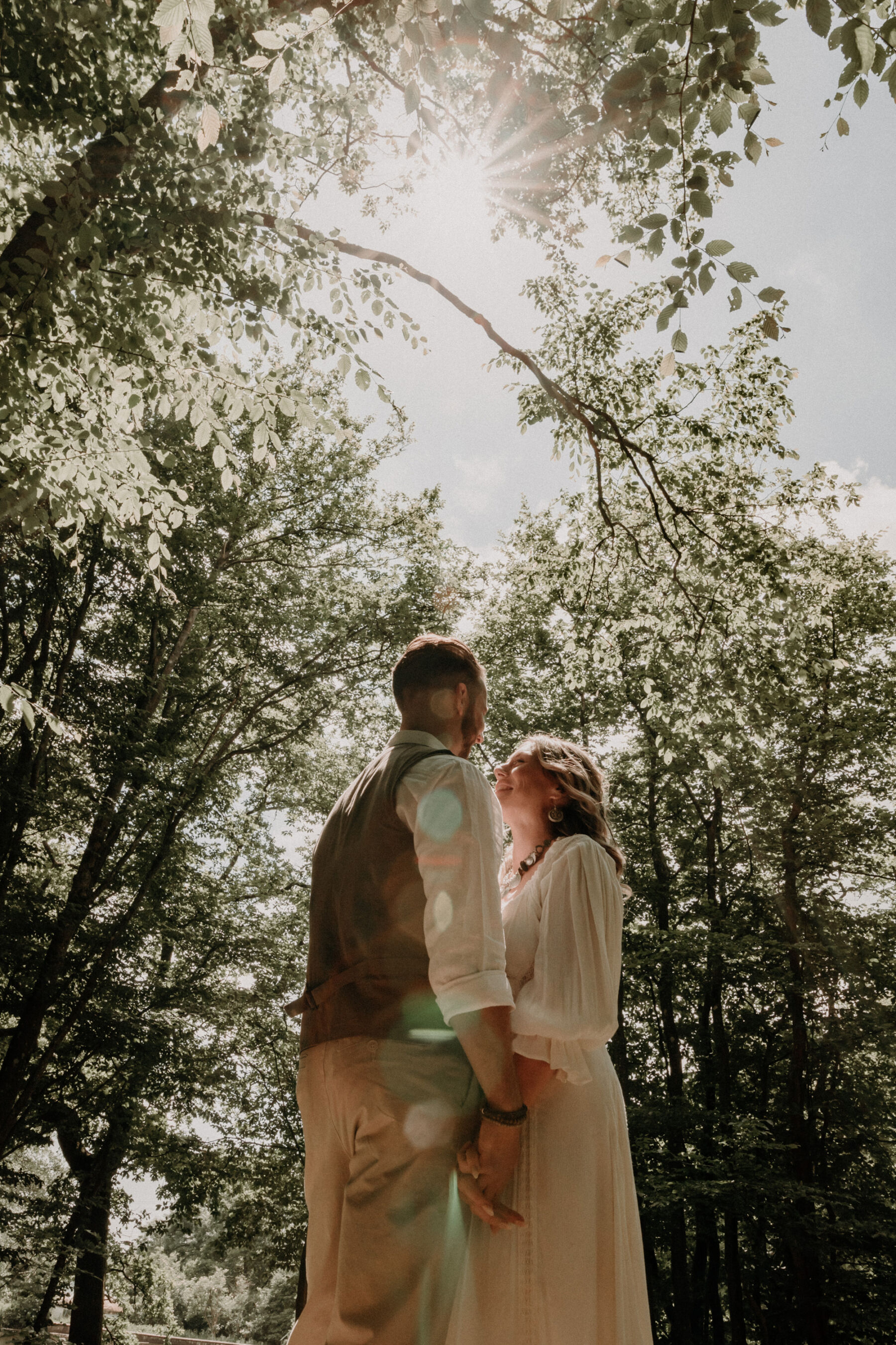 Wickerwood Farm, an Eco Friendly, Glamping Wedding Venue in East Sussex 9 Bride and groom standing beneath the dappled light streaming through a canopy of tree branches.