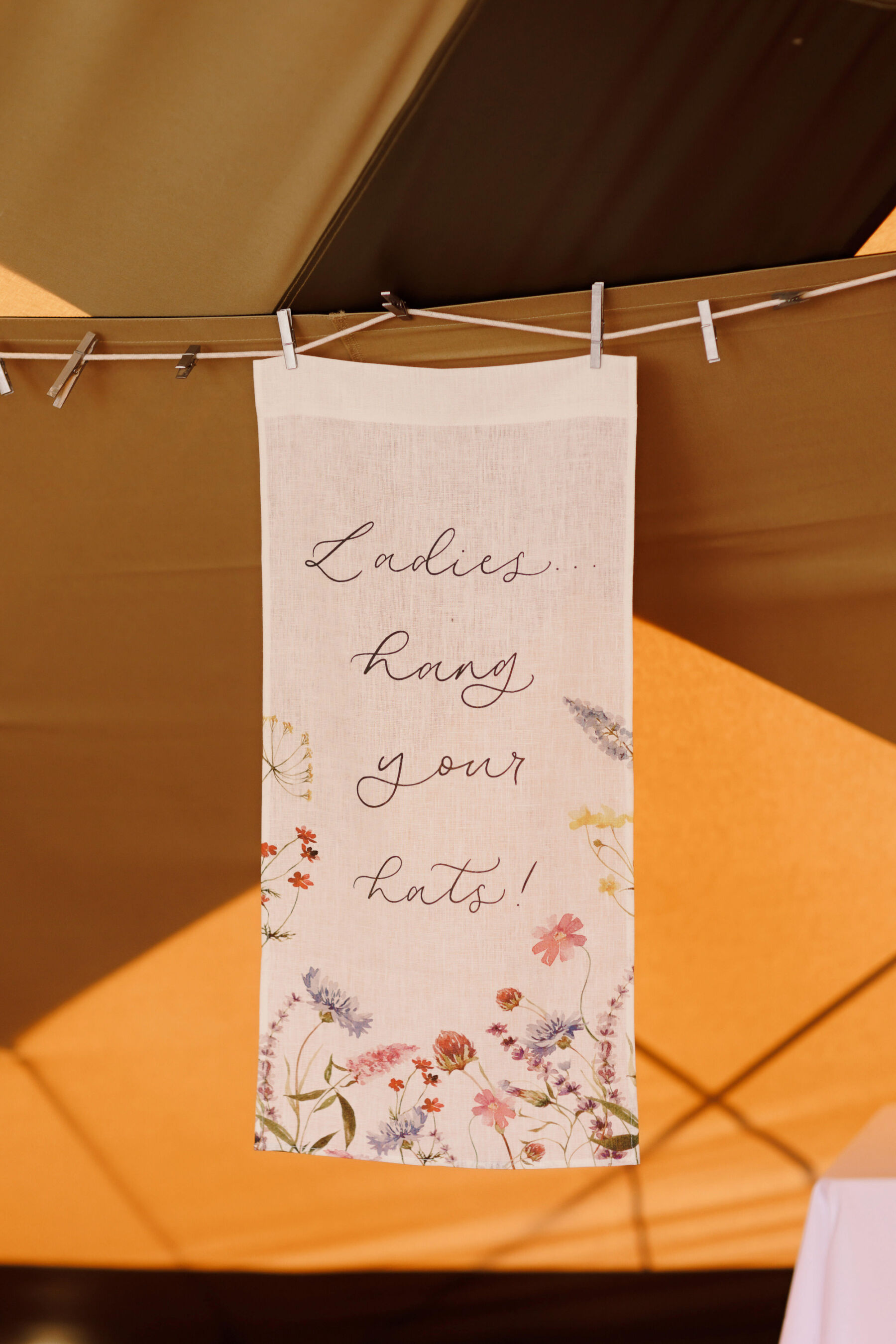 Ladies hang your hats! A fabric sign at a wedding hanging on a clothes line with pegs for the ladies to hang their heads on when they are dancing. 